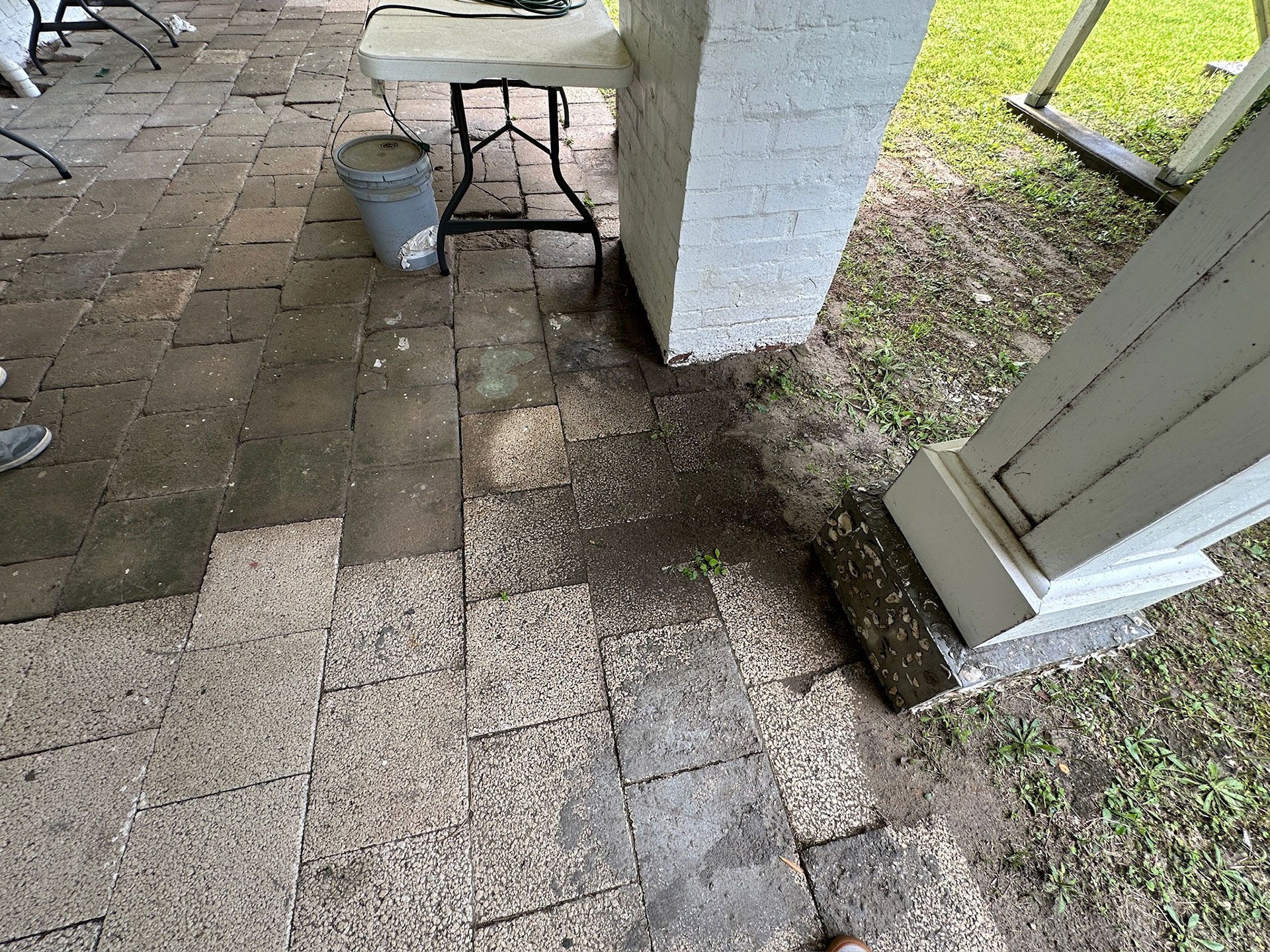 Outdoor patio with wet pavers, a bucket, and a white column beside a doorway