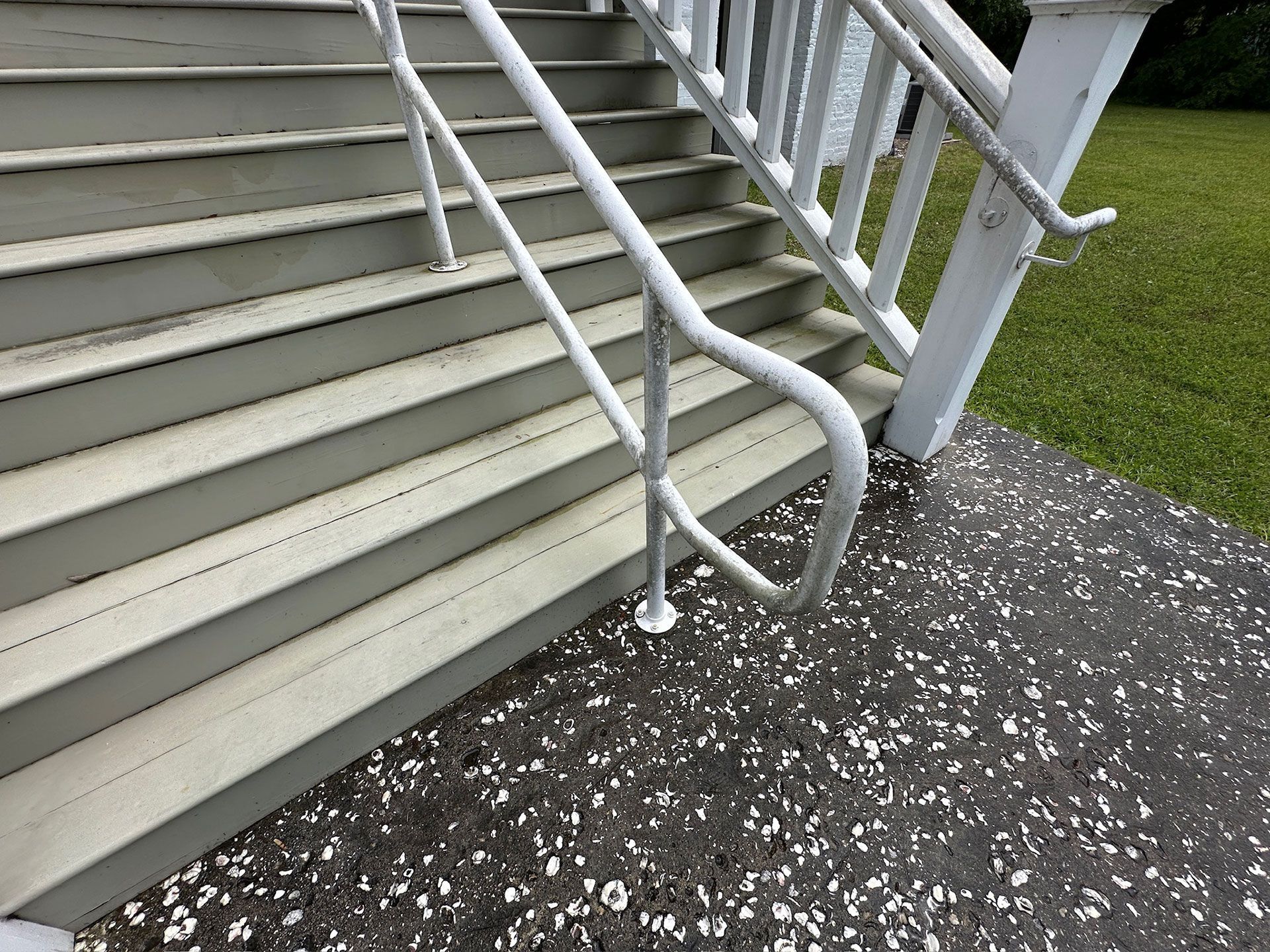 White handrail beside outdoor stairs over a speckled gravel path near green grass.