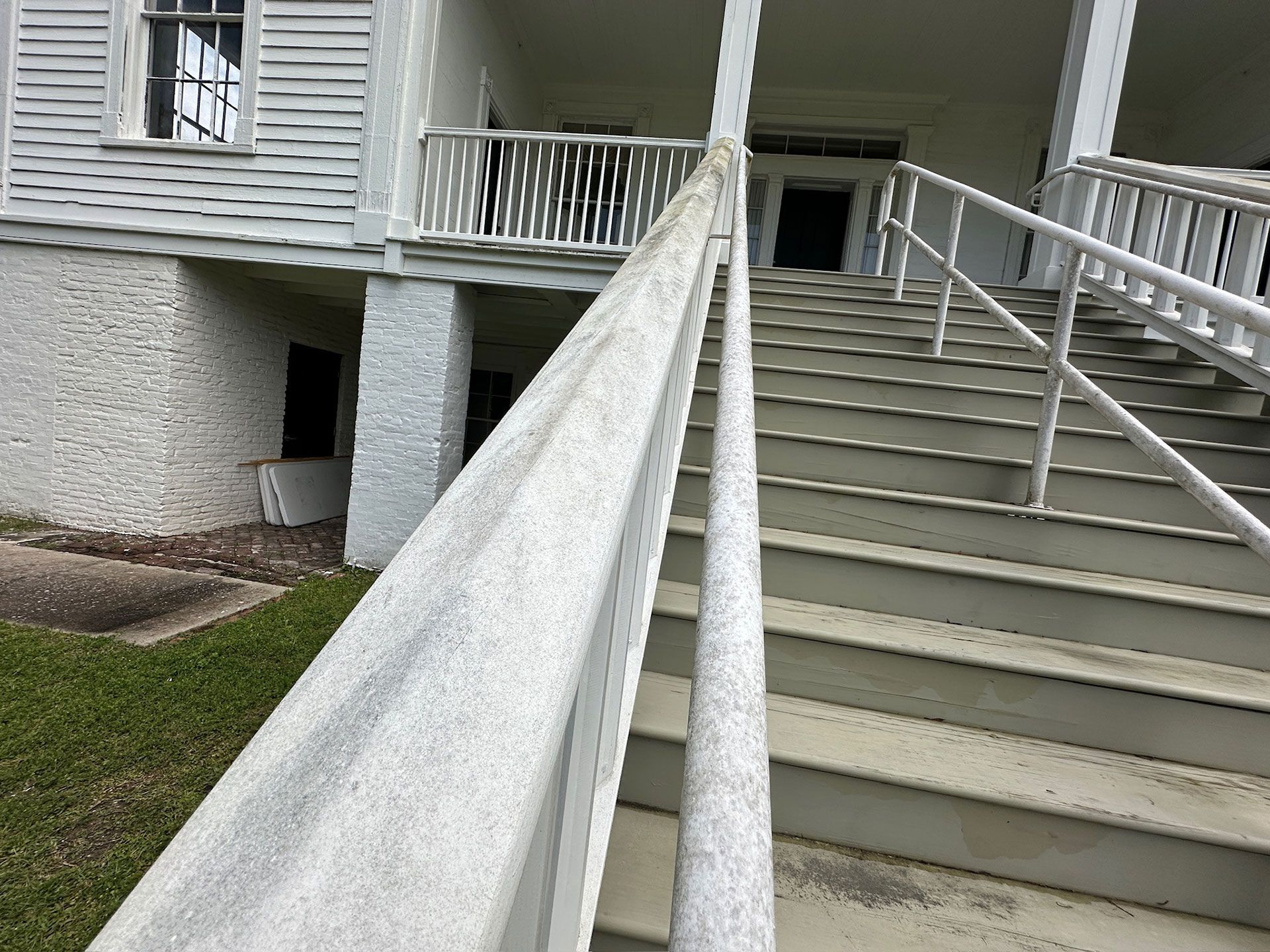 White stairway and ramp with railings leading to a building entrance beside a grassy area.