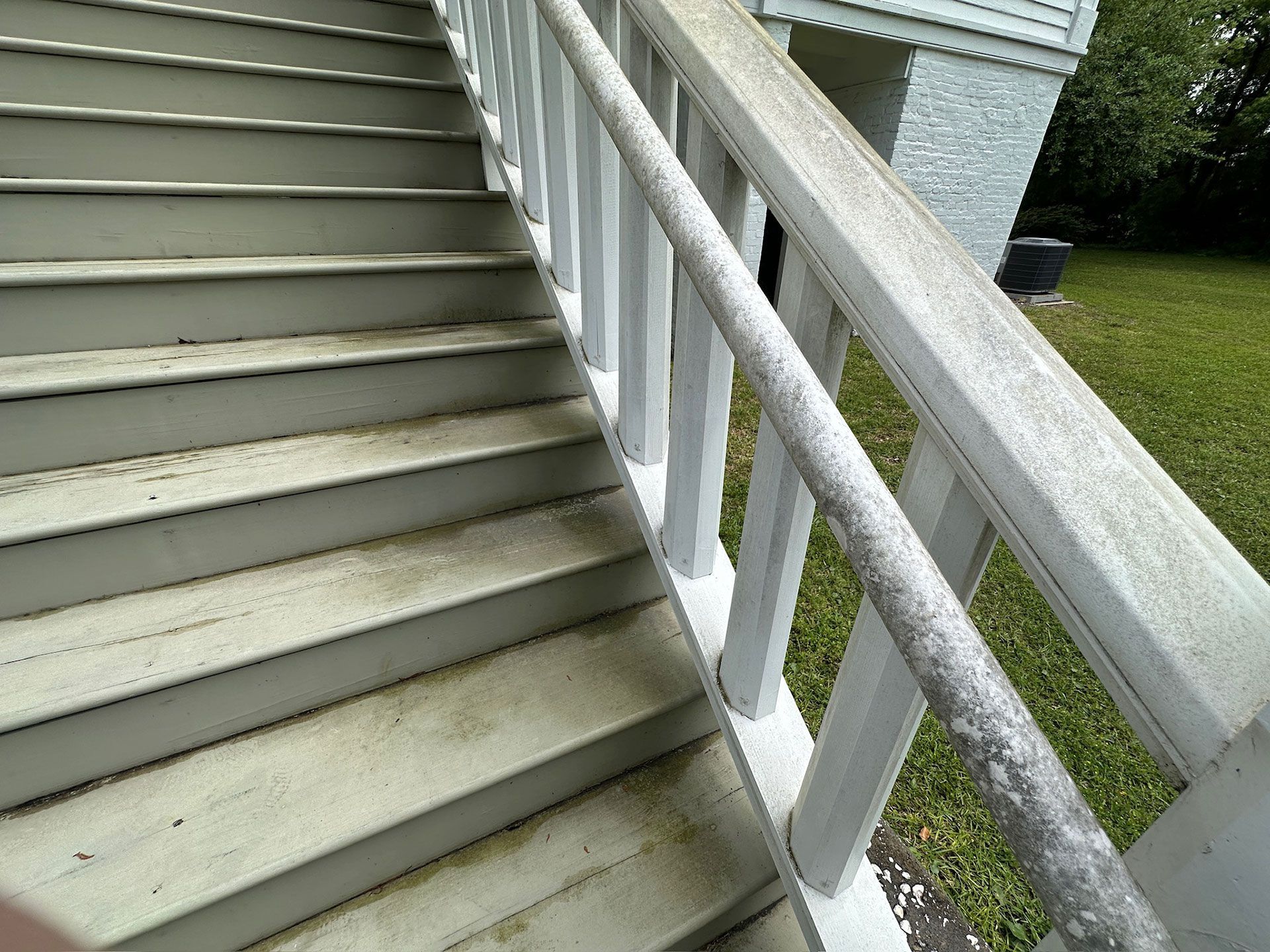 Exterior staircase with gray steps and white railing beside a house and lawn