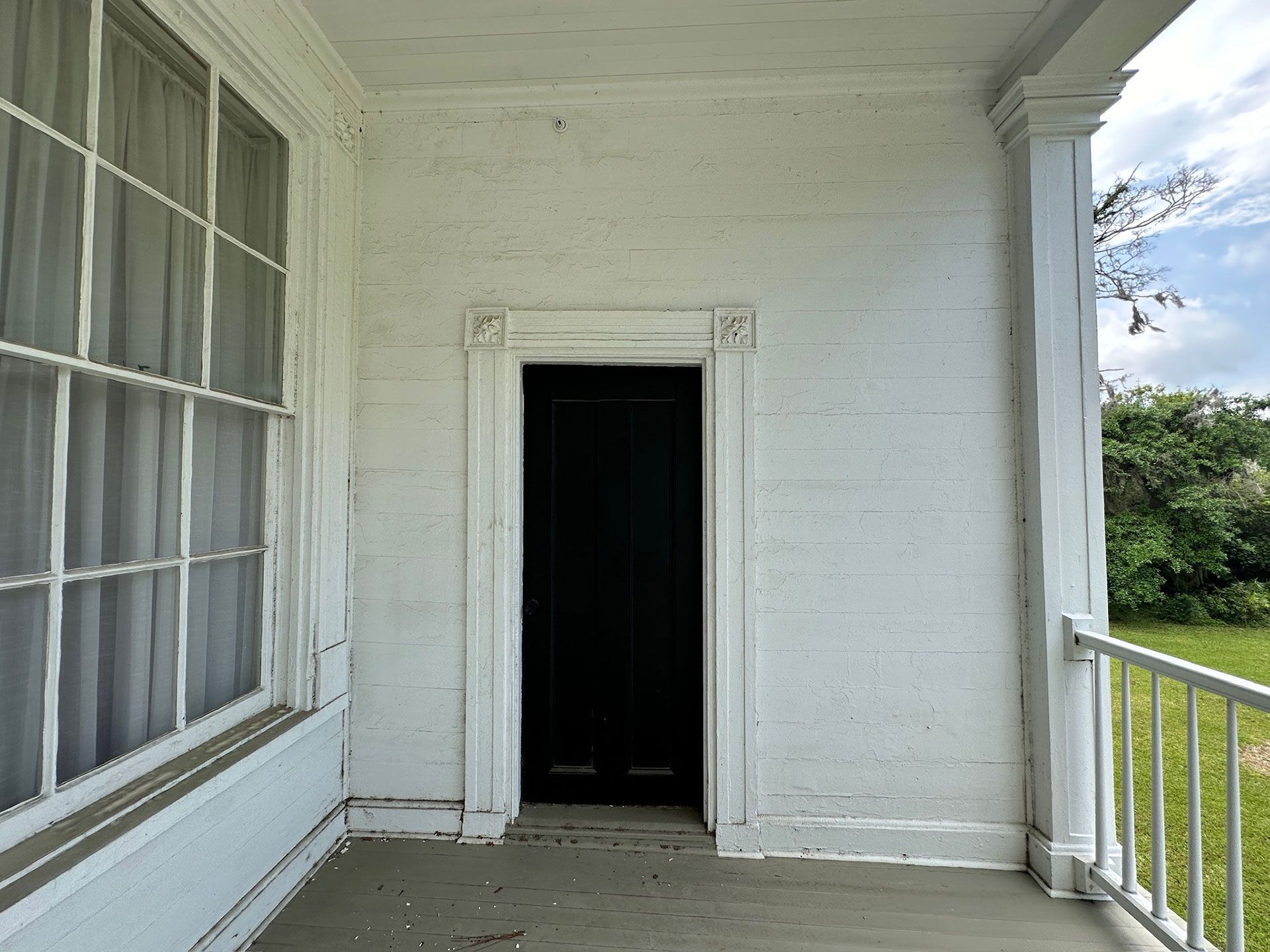 White porch with a dark open doorway, window on the left, and railing on the right.