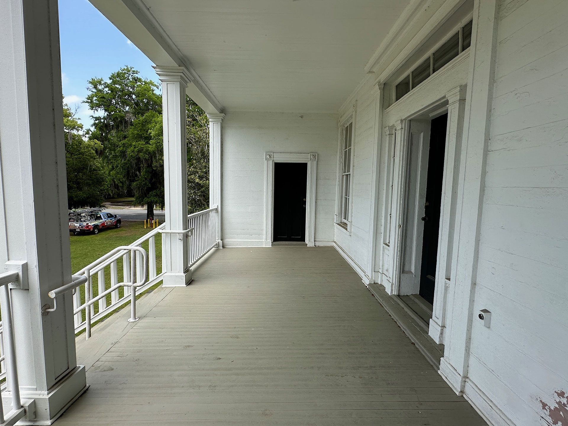 Covered porch with white railing, columns, and open doorway along a white house.