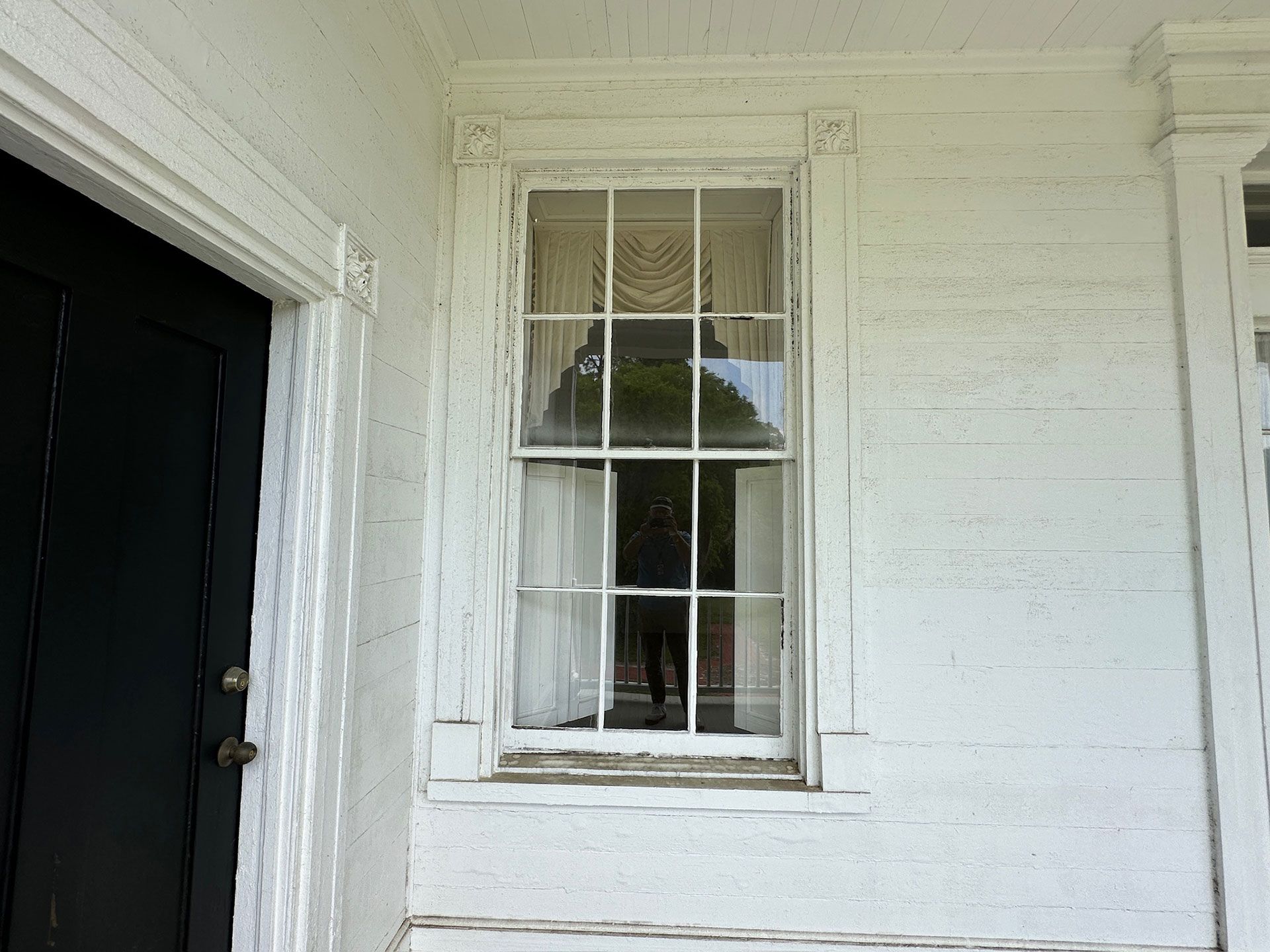 White exterior house wall with a small window and open black doorway on the left