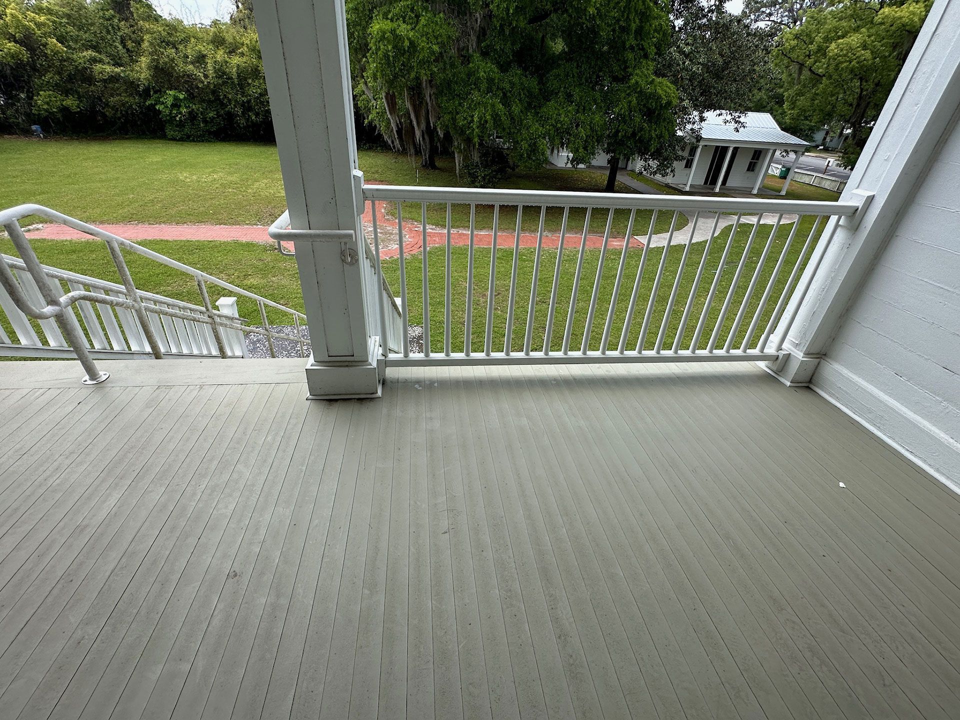 Porch overlooking a green yard and path, with white railing and gray floorboards.