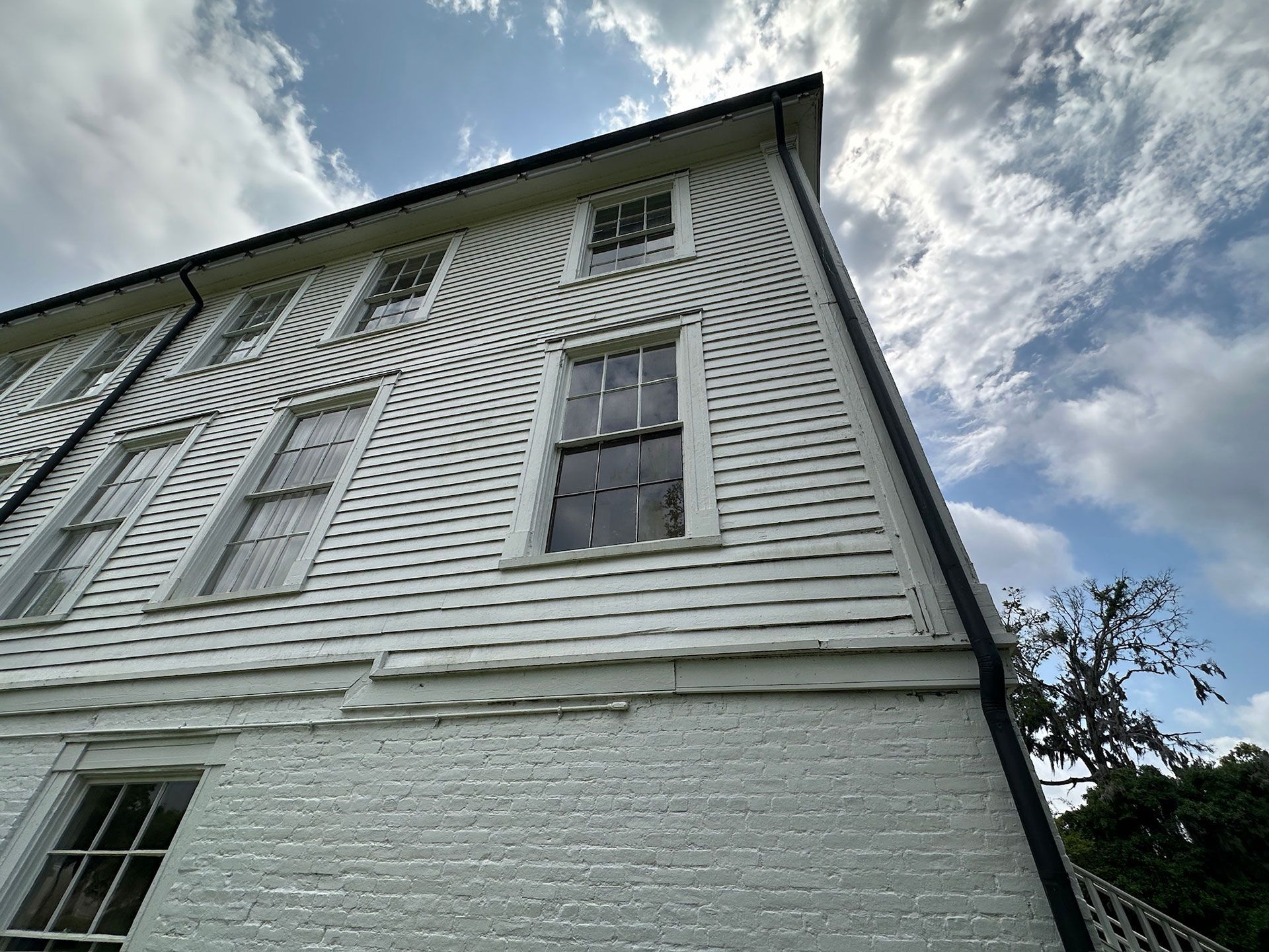 Low-angle view of a white clapboard house with tall windows against a cloudy sky