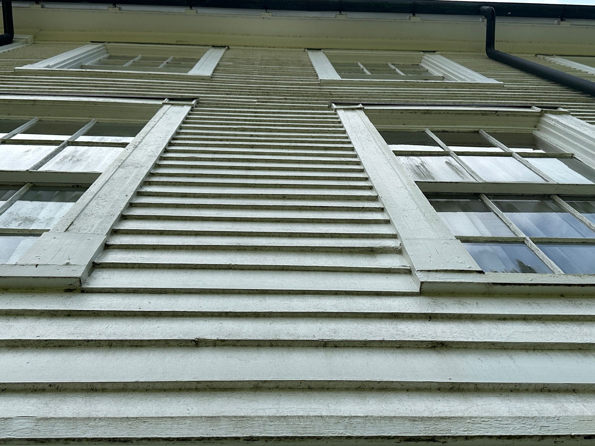 Low-angle view of a building facade with white siding, windows, and a steep central roofline