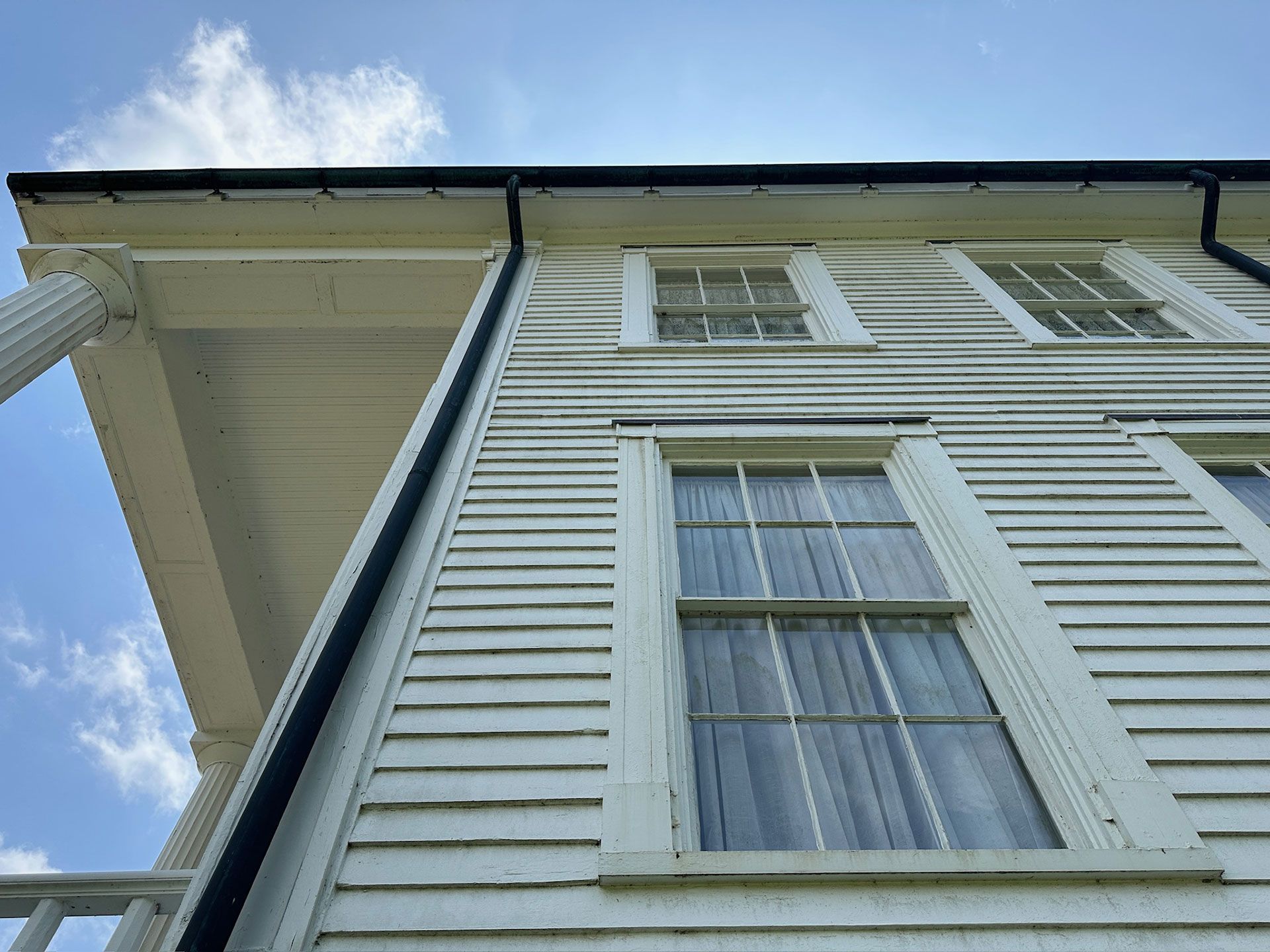 White house exterior with vertical siding, windows, and roofline against a blue sky