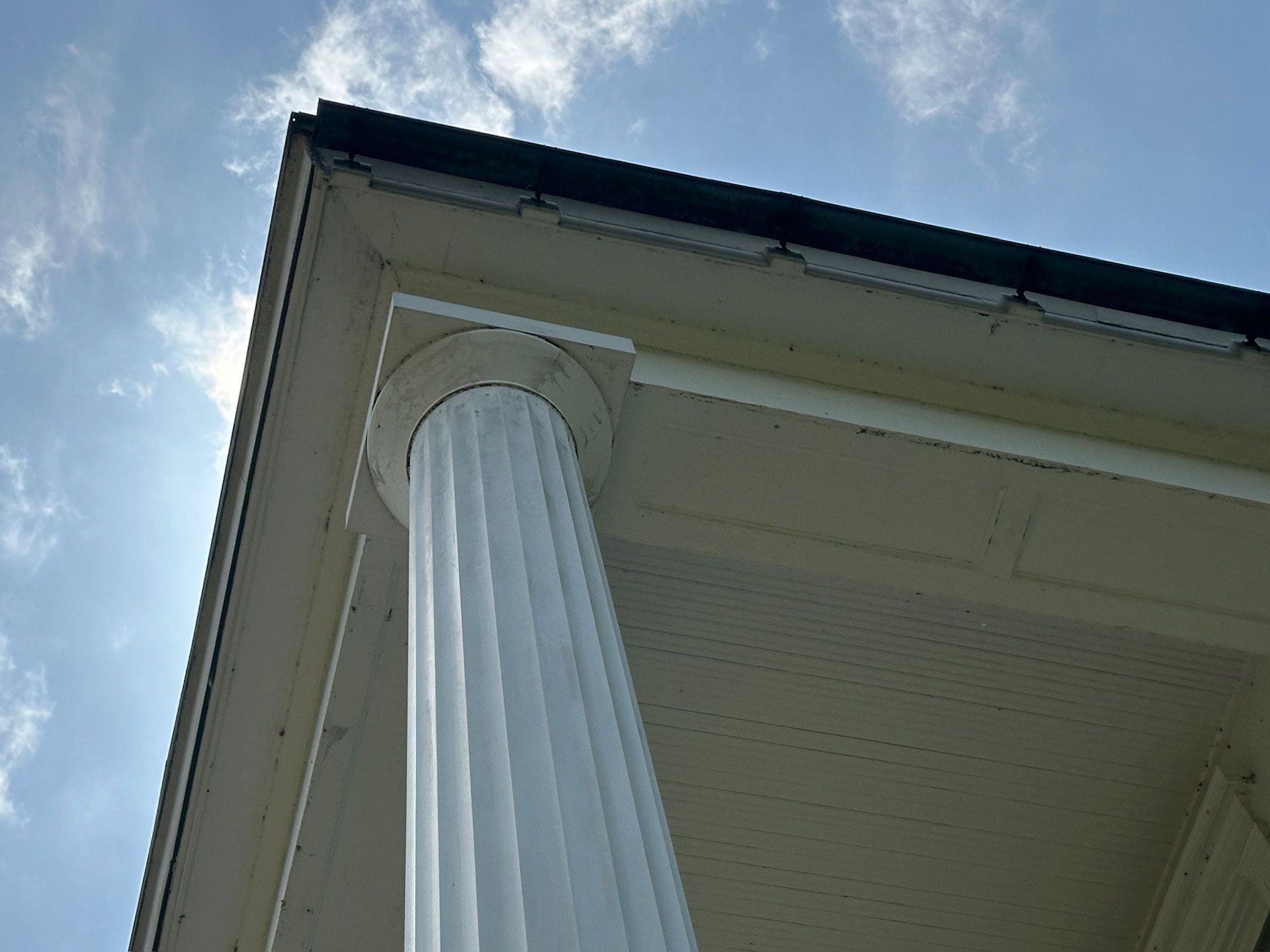 White fluted column supporting a house roof against a cloudy blue sky