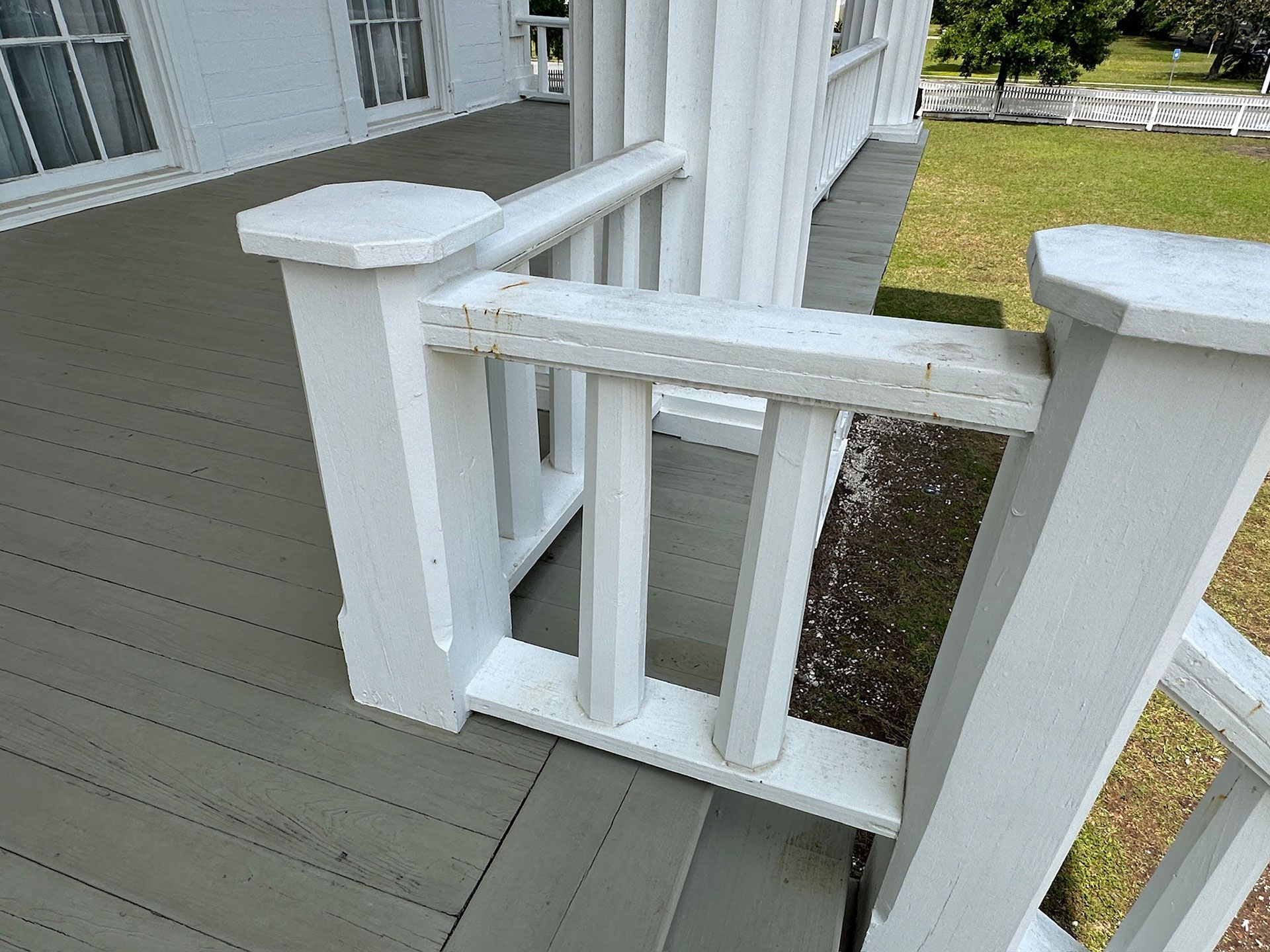 White porch gate with horizontal railings on a gray deck beside a house and lawn.