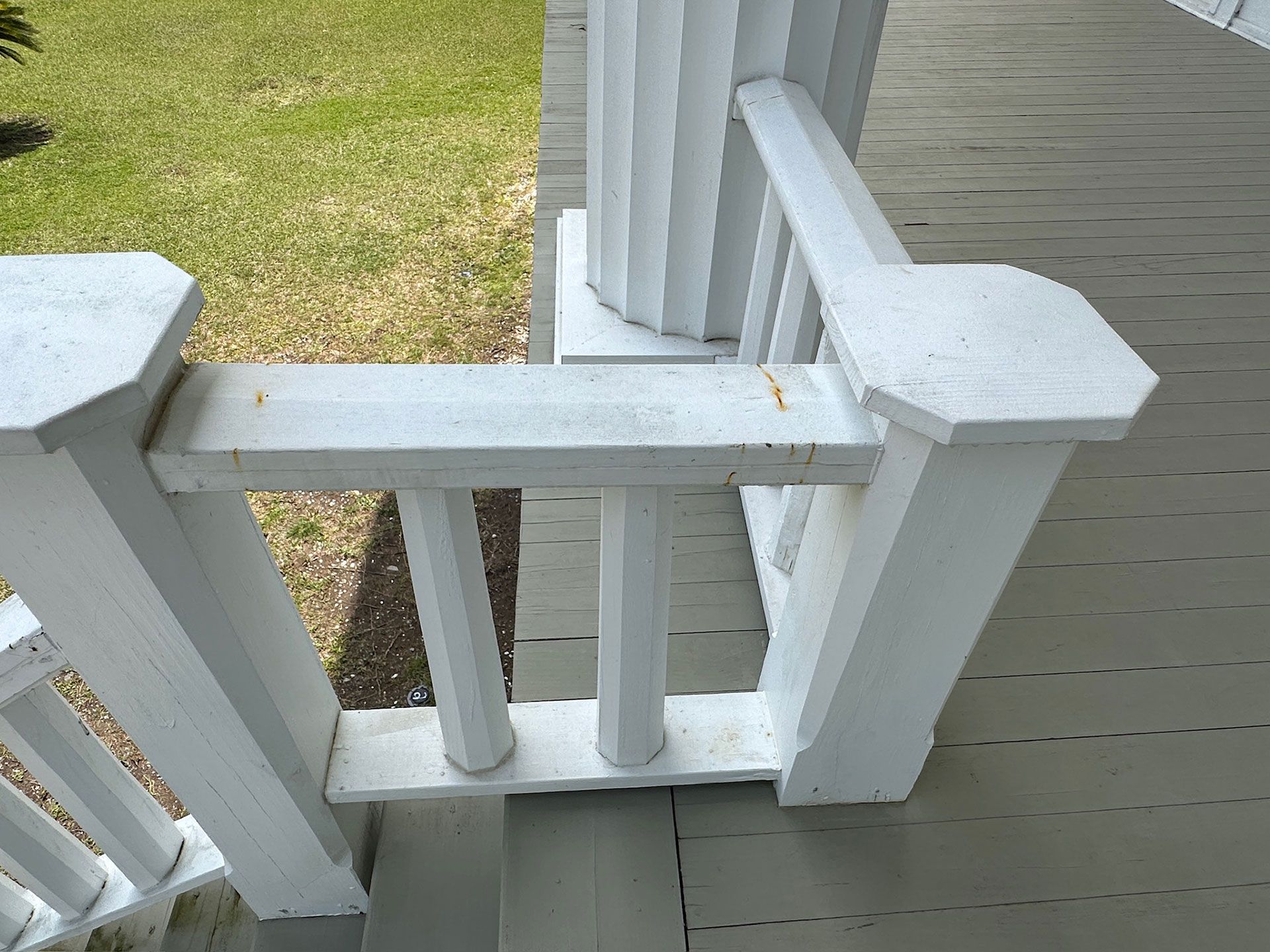 White porch railing and stair landing beside a grassy yard and gray house siding.