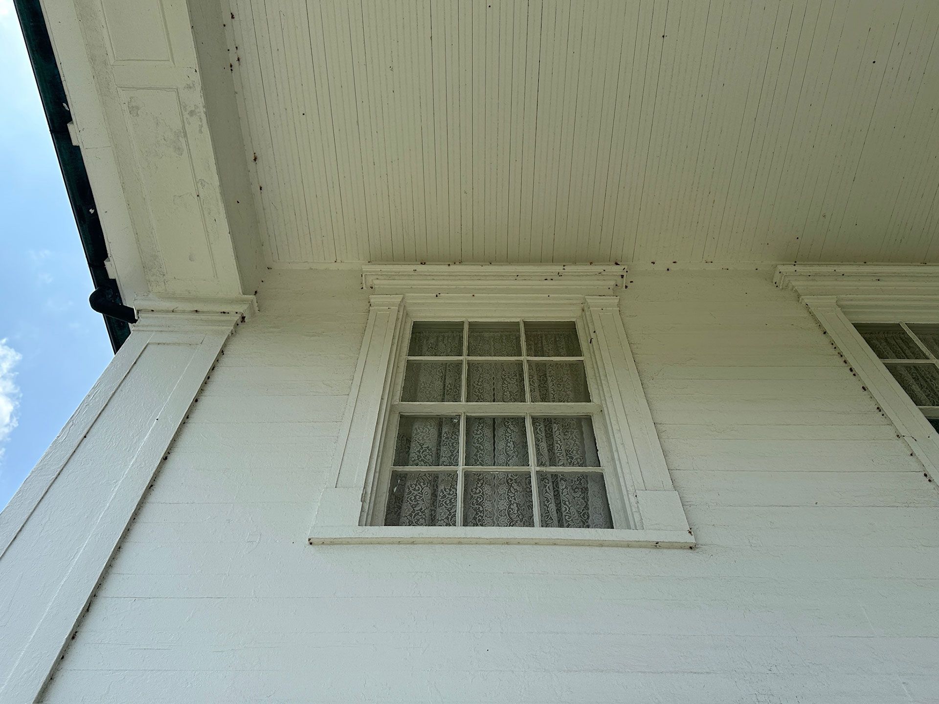 White house exterior with a small window under the eaves and blue sky at the left edge