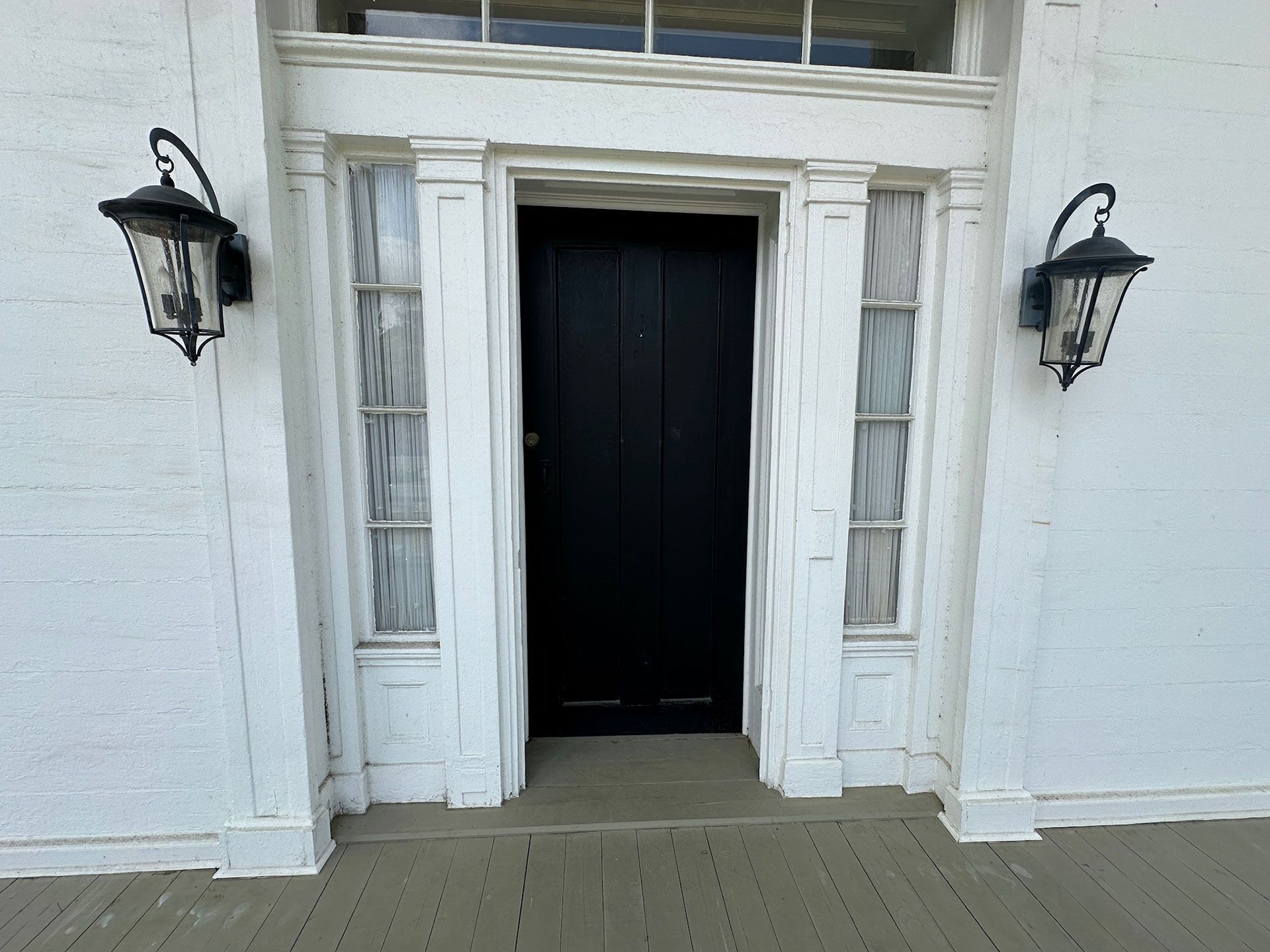 White building entrance with black double doors and two lantern-style wall lights