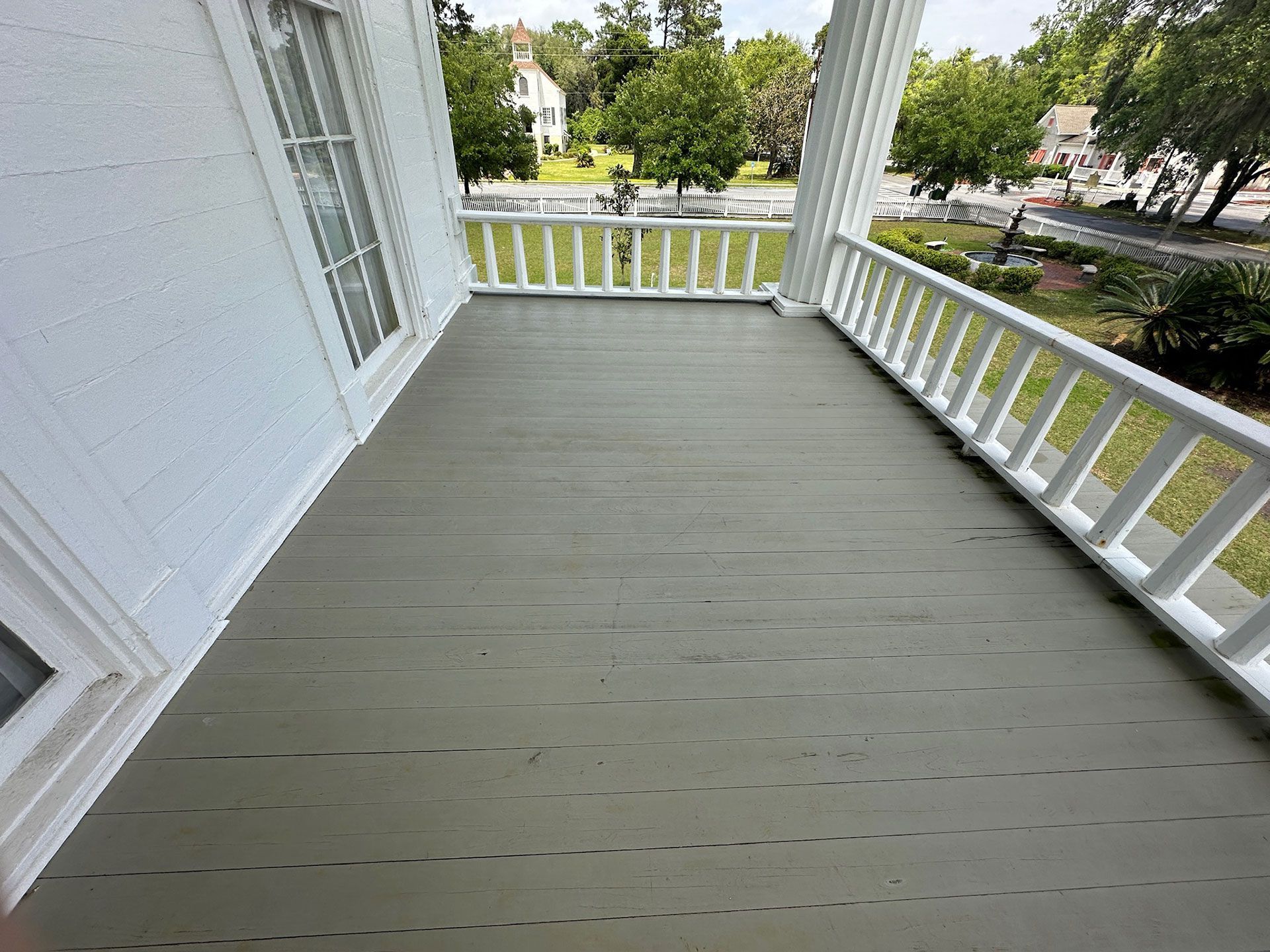 White porch with gray painted floor, white railing, and a view of trees and street beyond.