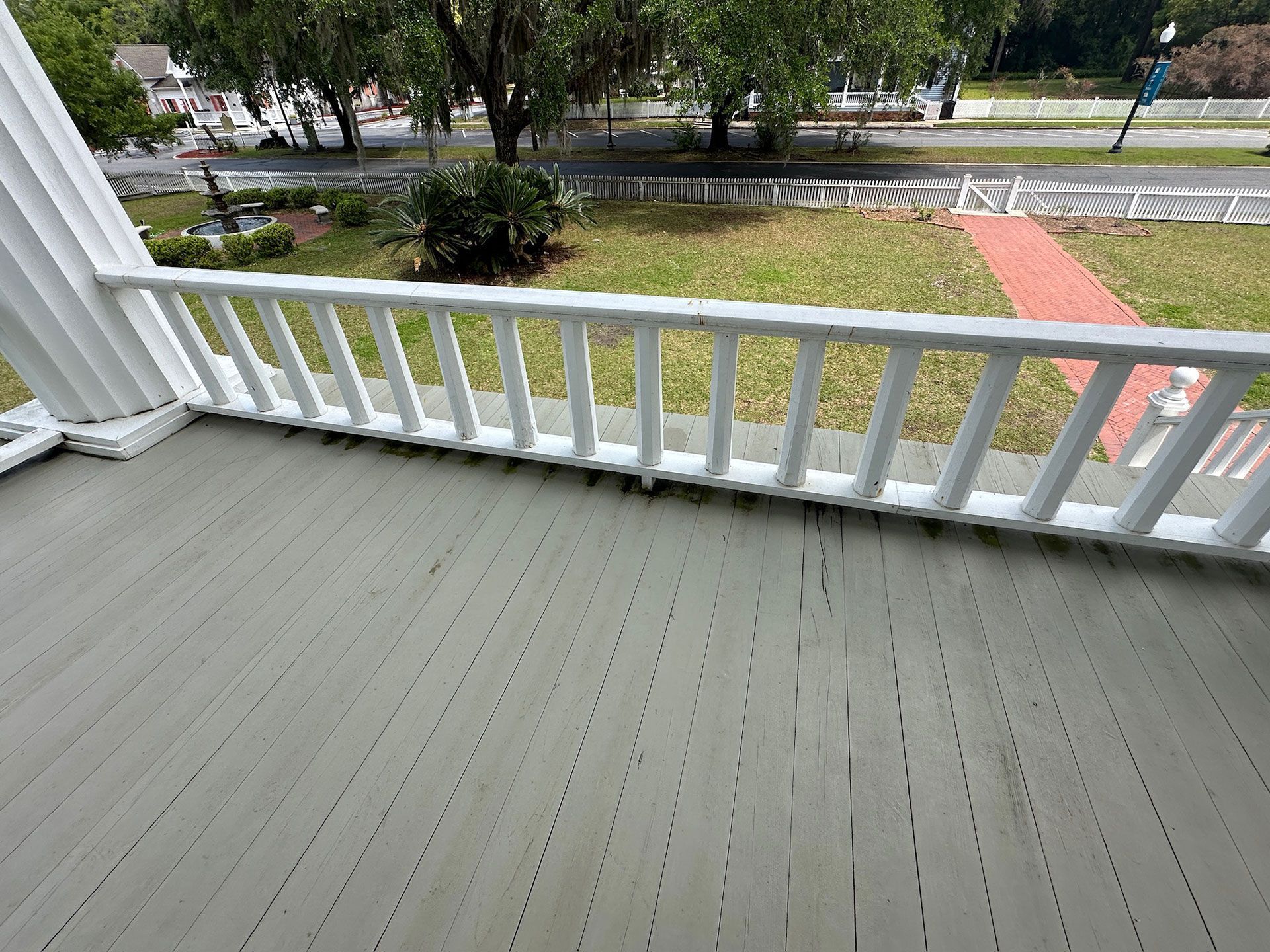 Porch with gray floor, white railing, and a view of trees, road, and sidewalk beyond.