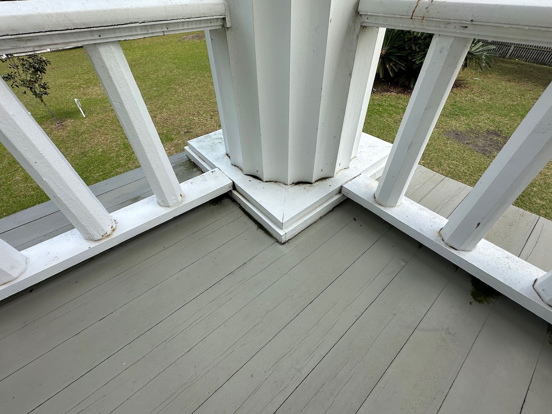 White porch railing and central column on a gray wooden deck corner