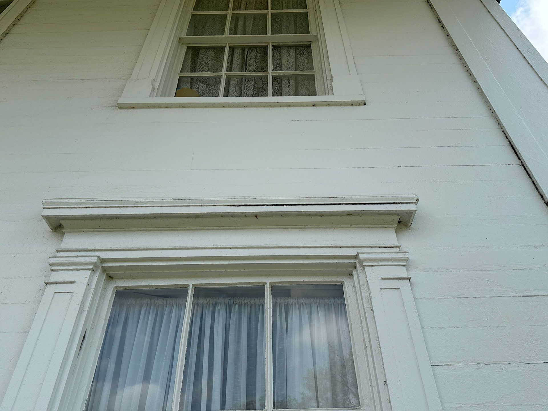 White house exterior with two windows and decorative trim under a sloped roof