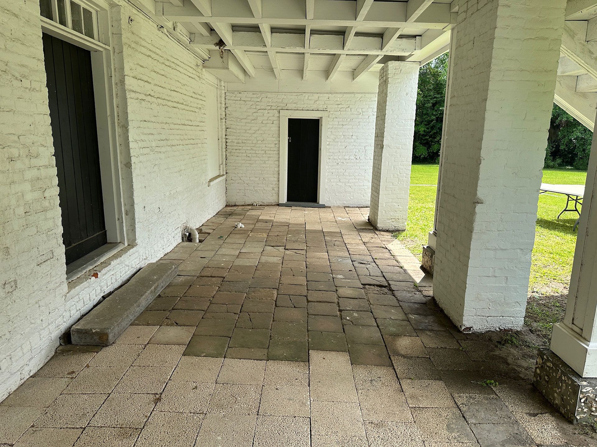 Covered white porch with brick floor, square columns, and an open doorway.