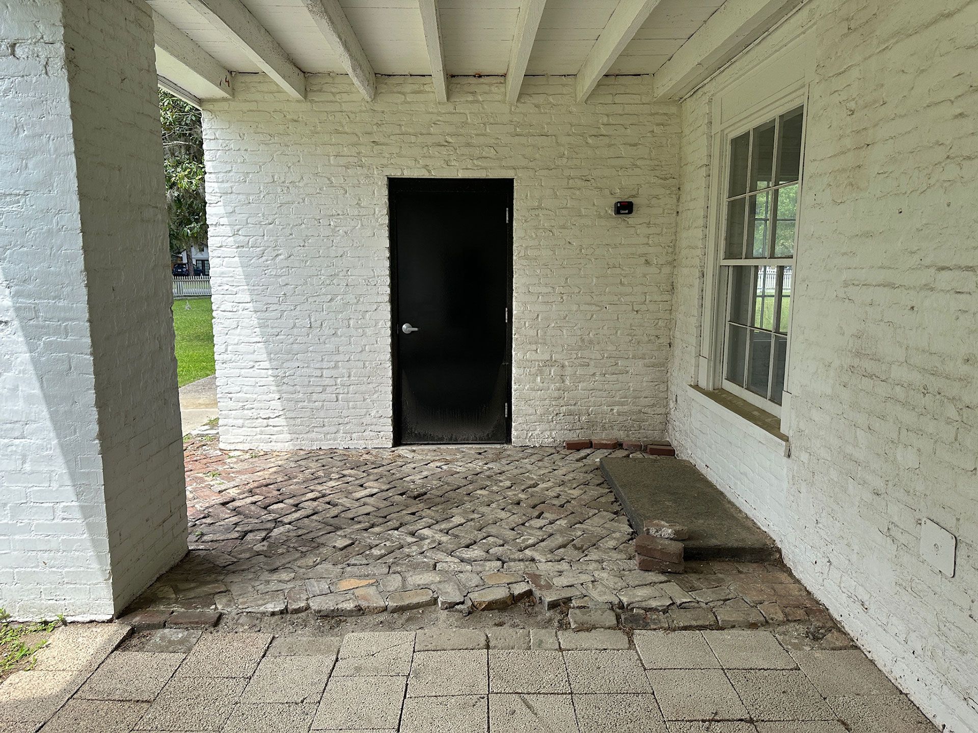 Covered white brick porch with cracked concrete floor and an open dark doorway.