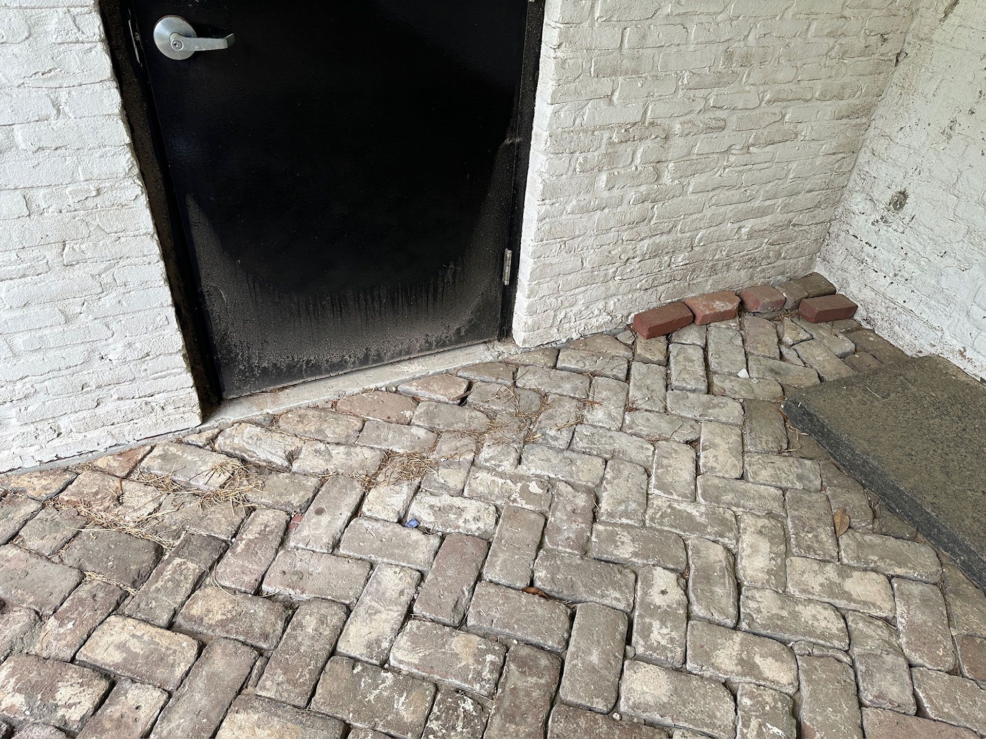 Brick-paved ramp leading to a dark doorway beside a white wall
