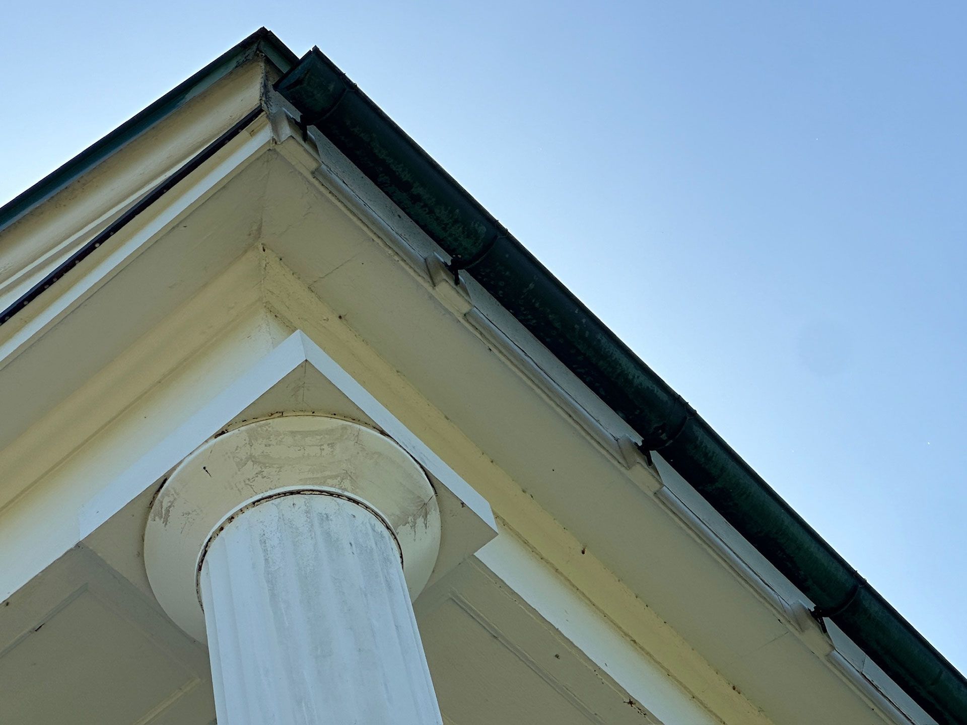 White column supporting a house roof with cream siding and blue sky above