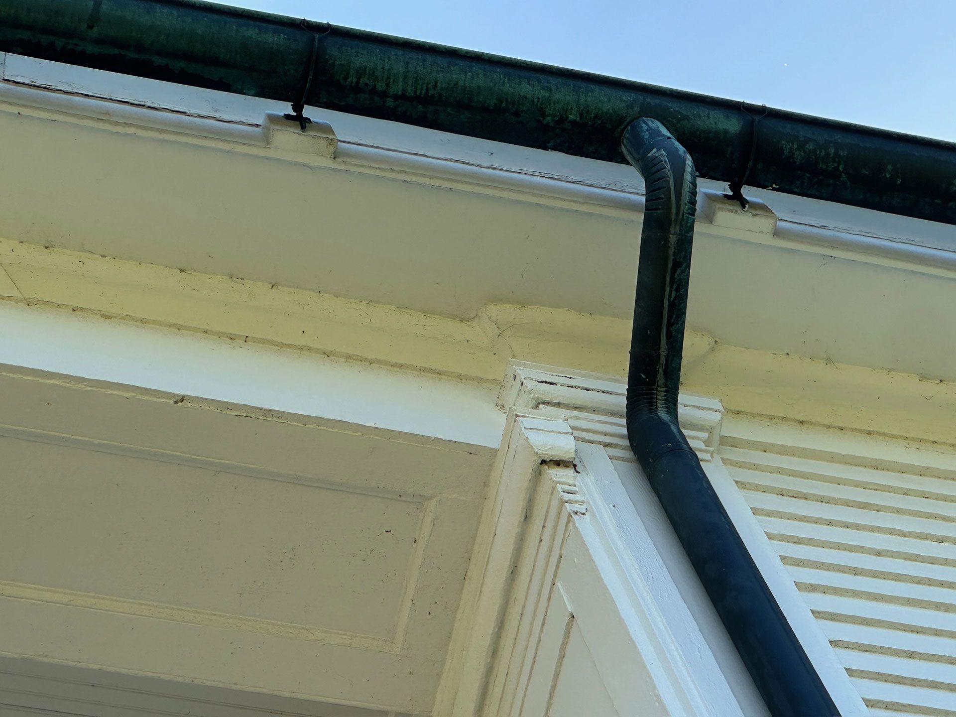 Gutter downspout attached to the roof edge of a cream-colored house