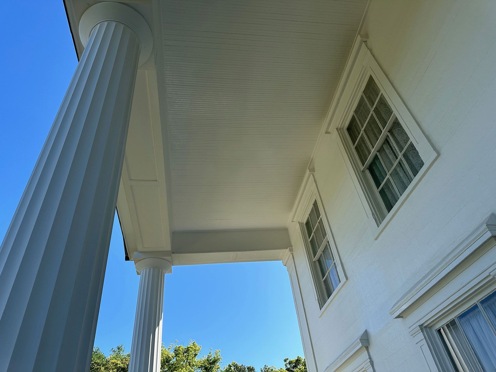 White house porch with tall fluted columns and windows under a blue sky