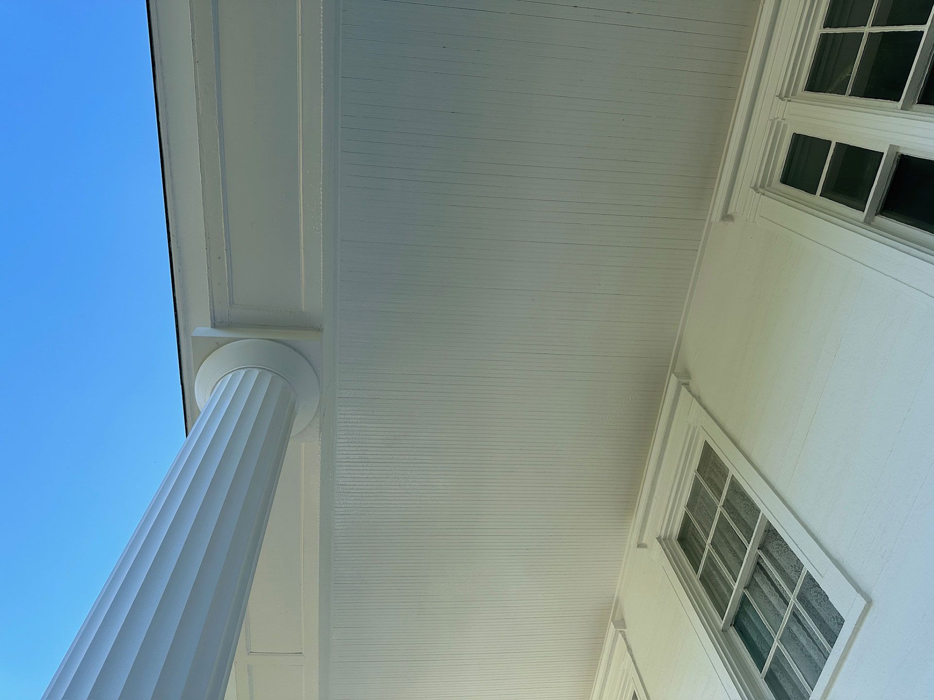 White house exterior with tall column and windows viewed from below against a blue sky