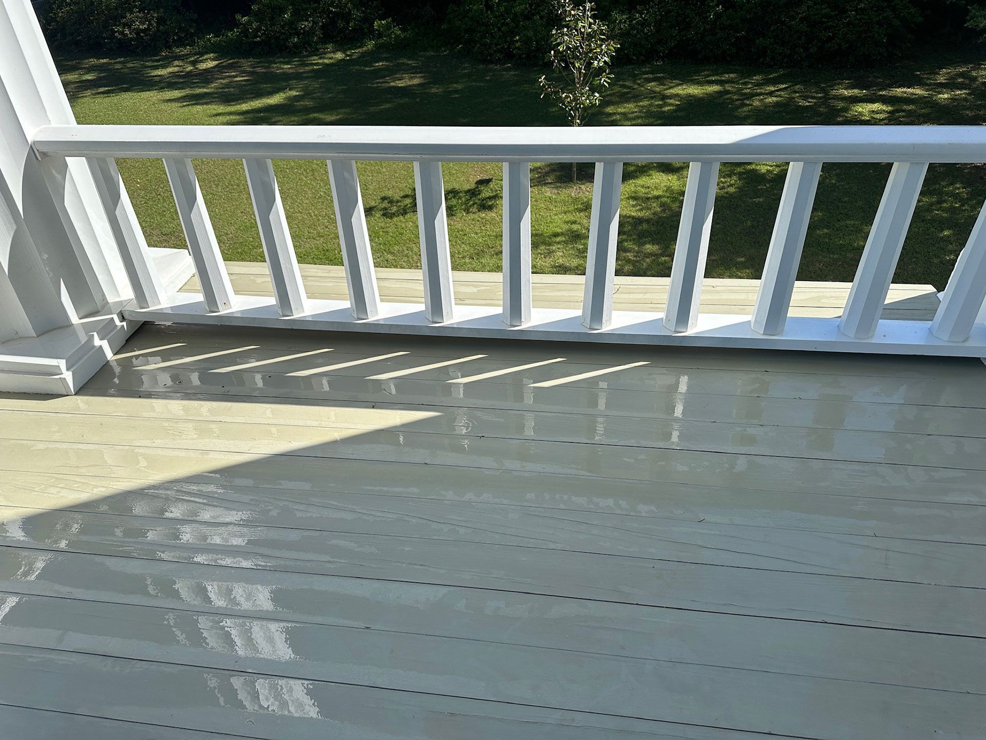 White porch deck with railing casting shadows in bright sunlight, overlooking a green yard