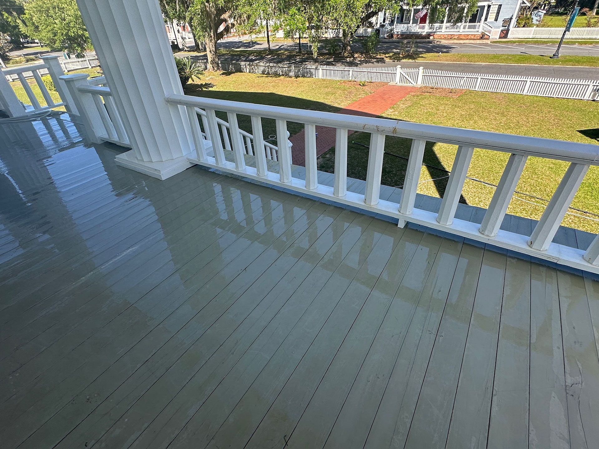 Front porch with white railings, gray floor, and view of a street and grassy yard.