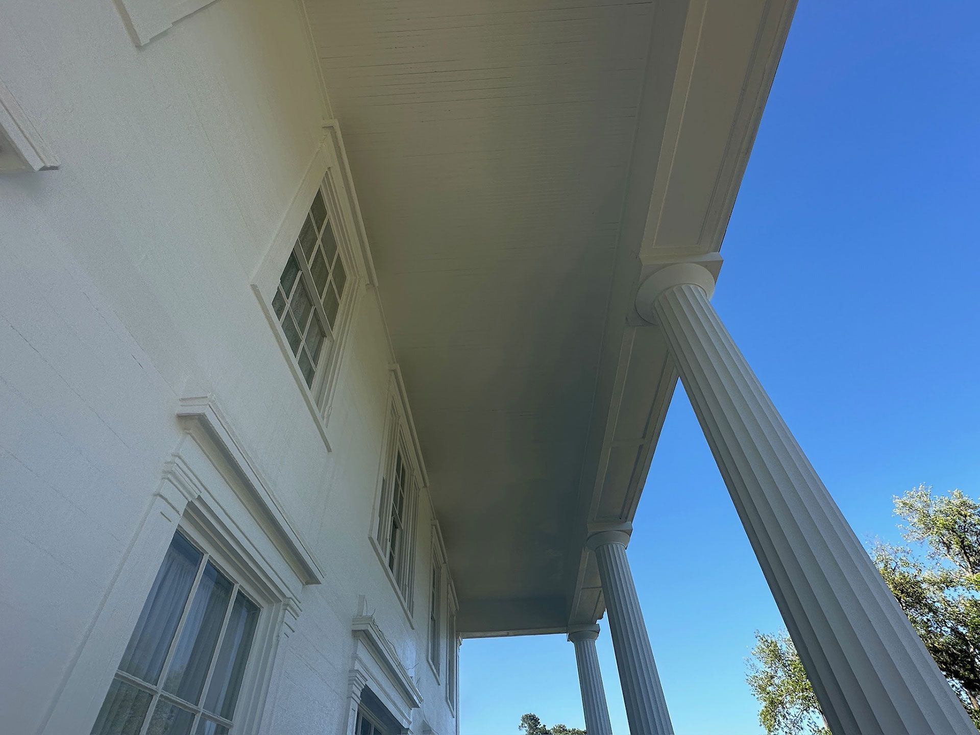 White house porch with tall columns, windows, and a blue sky above