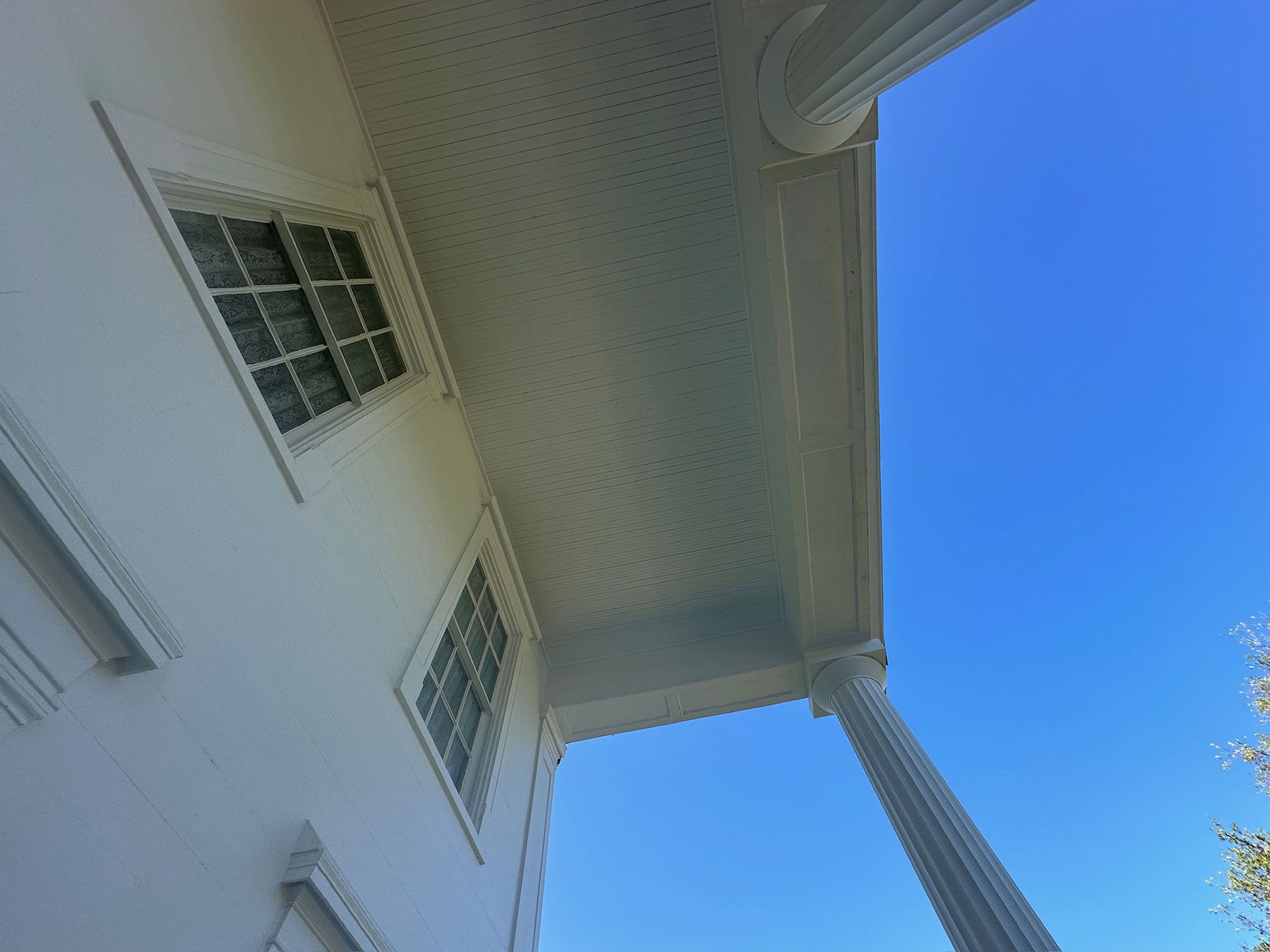 Upward view of a white house exterior with windows, porch column, and blue sky