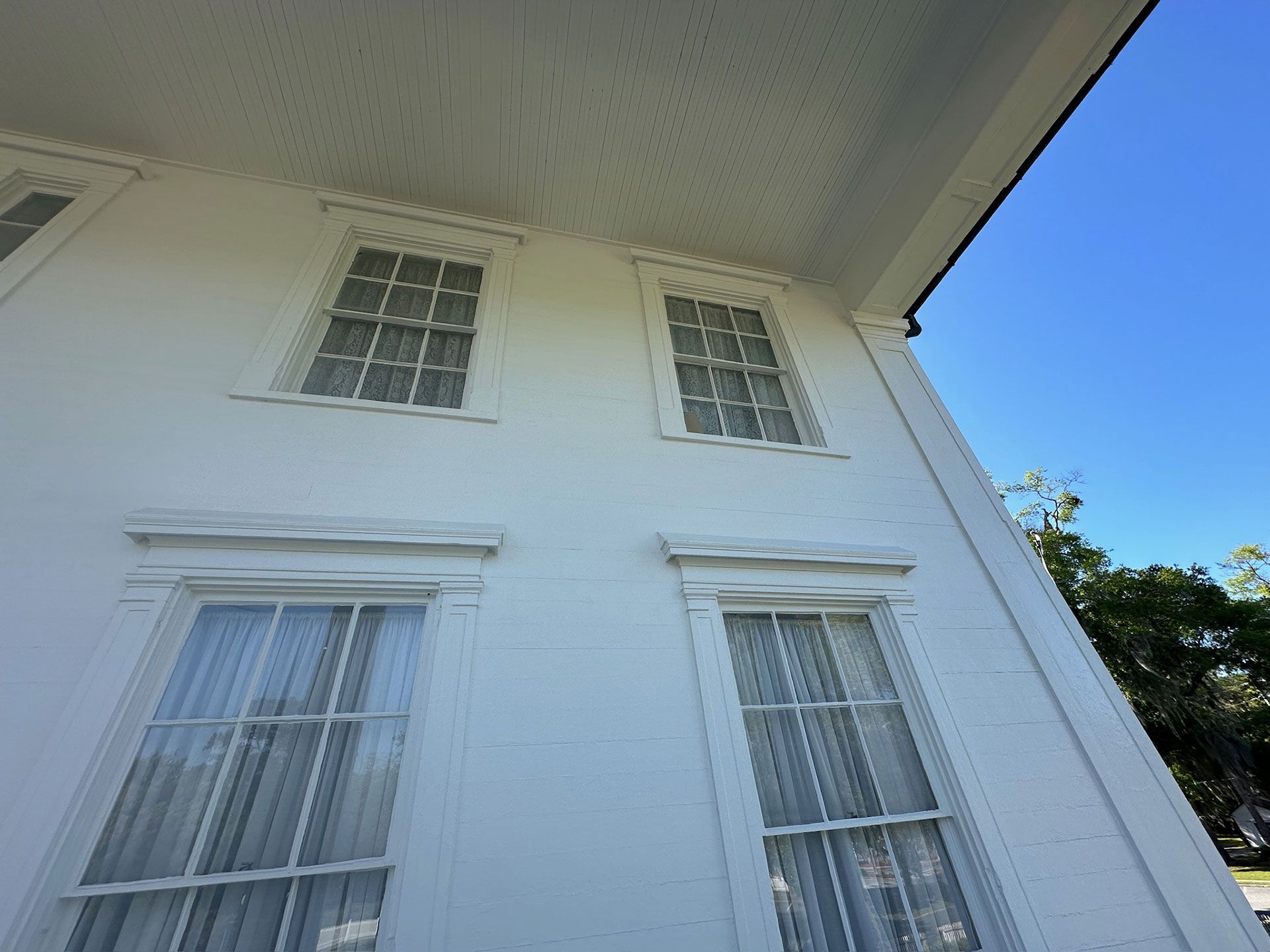 White house exterior with four windows, seen from below against a blue sky