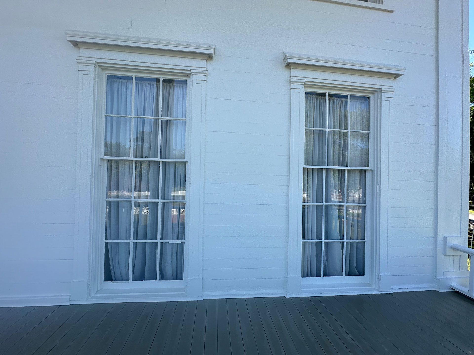 White building facade with two tall windows and a dark pavement in front