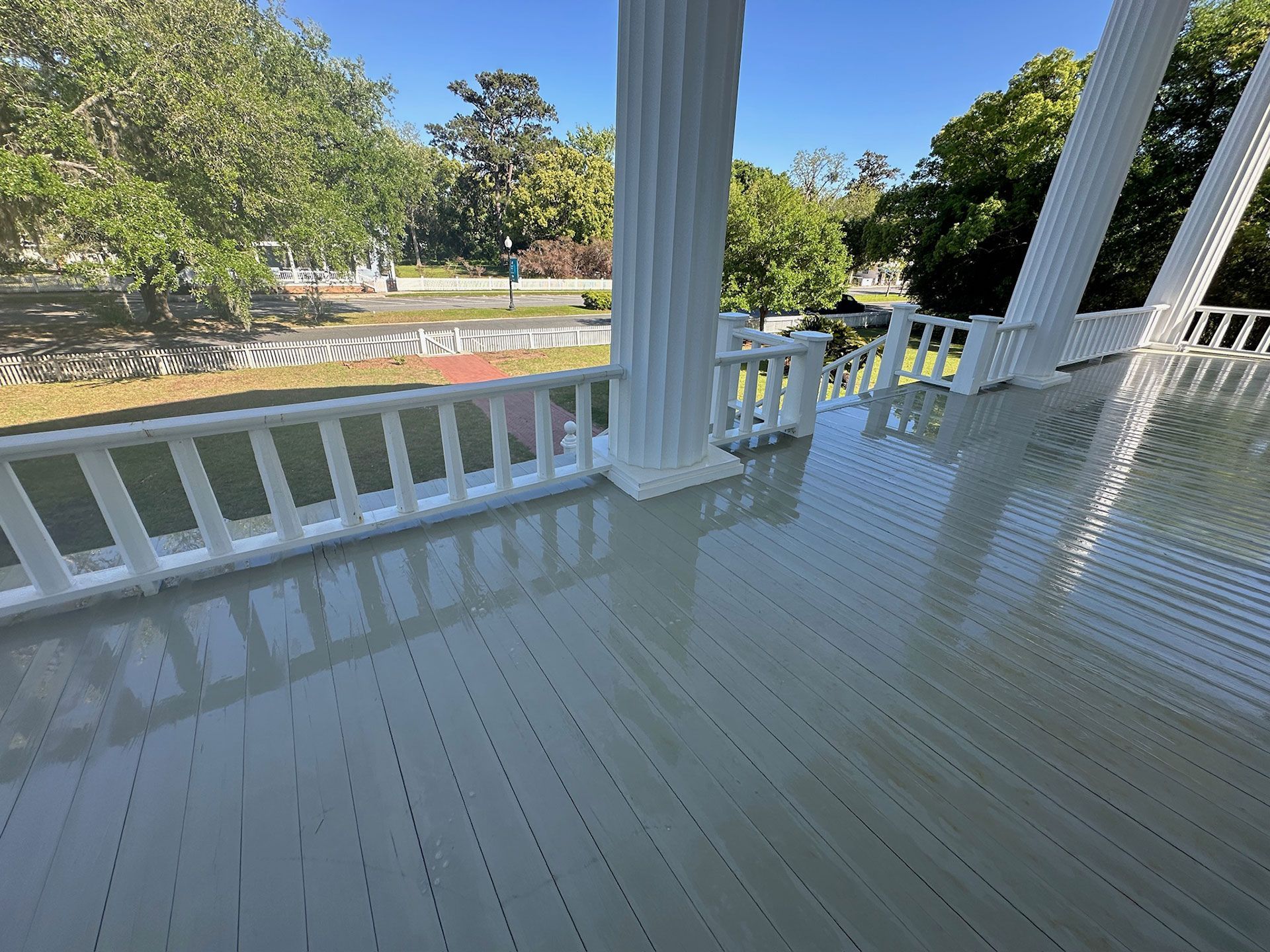 White porch with railings overlooking a sunny park and pond