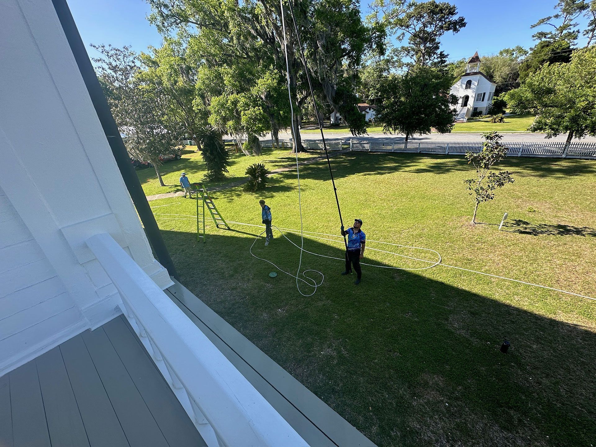 View from a porch to a grassy yard with two people standing near trees and a road.