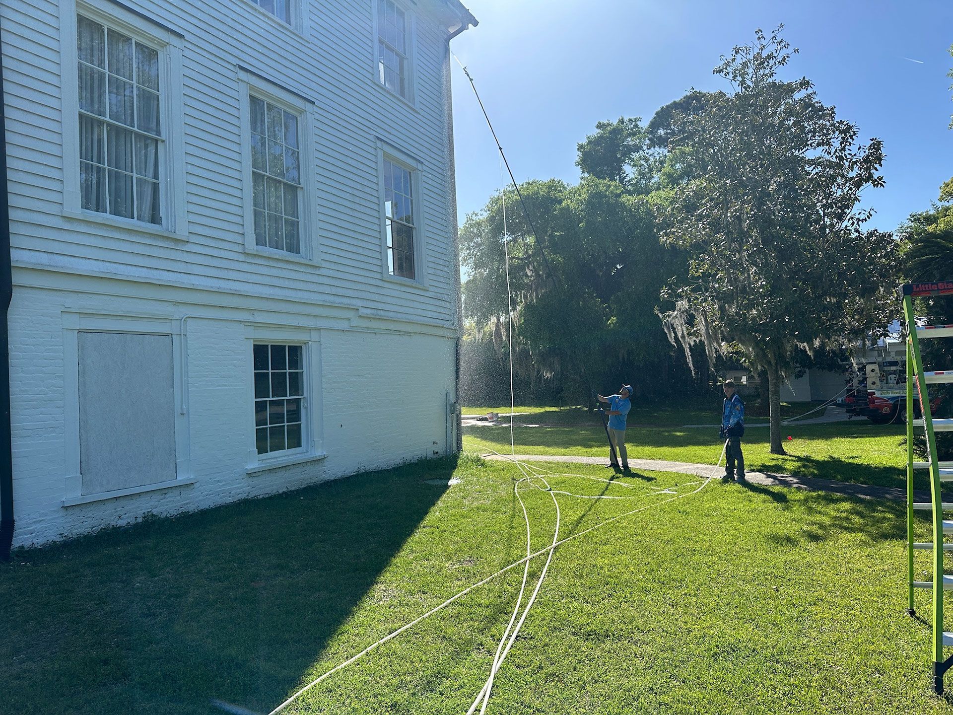 People on a sunny lawn beside a white building, with ropes or cables stretched across the grass.