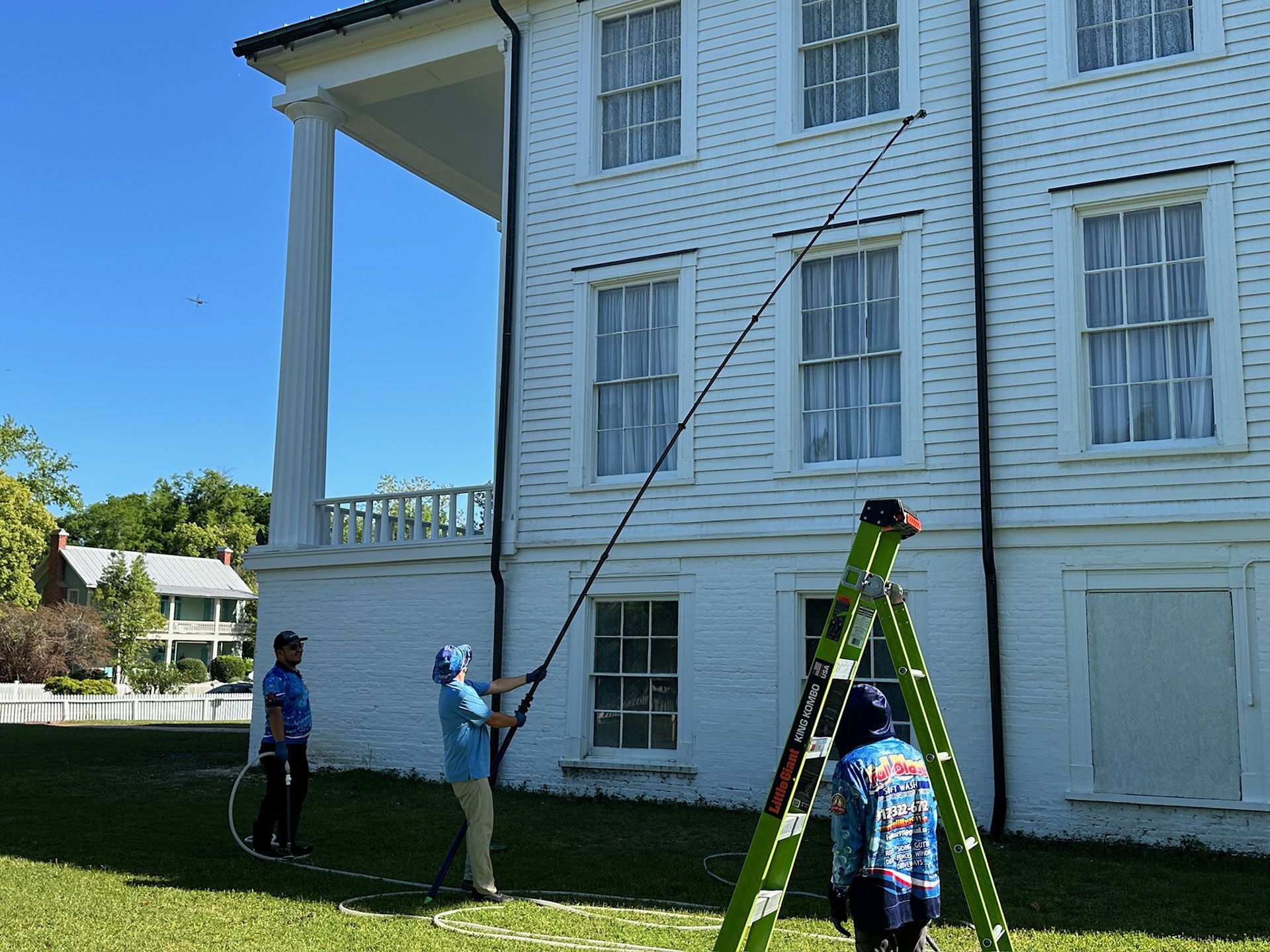 Workers on ladders painting a white house exterior under a blue sky