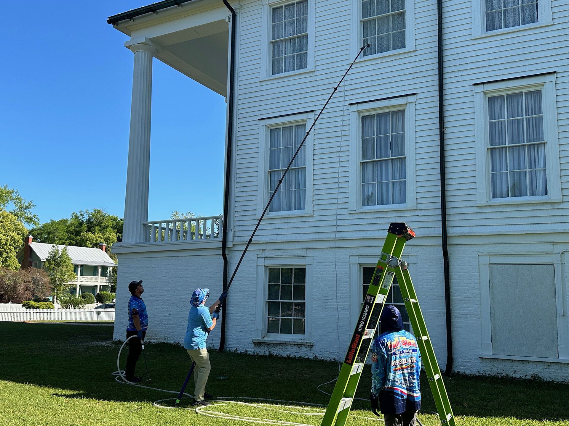 People painting the exterior of a white house using ladders on a sunny day
