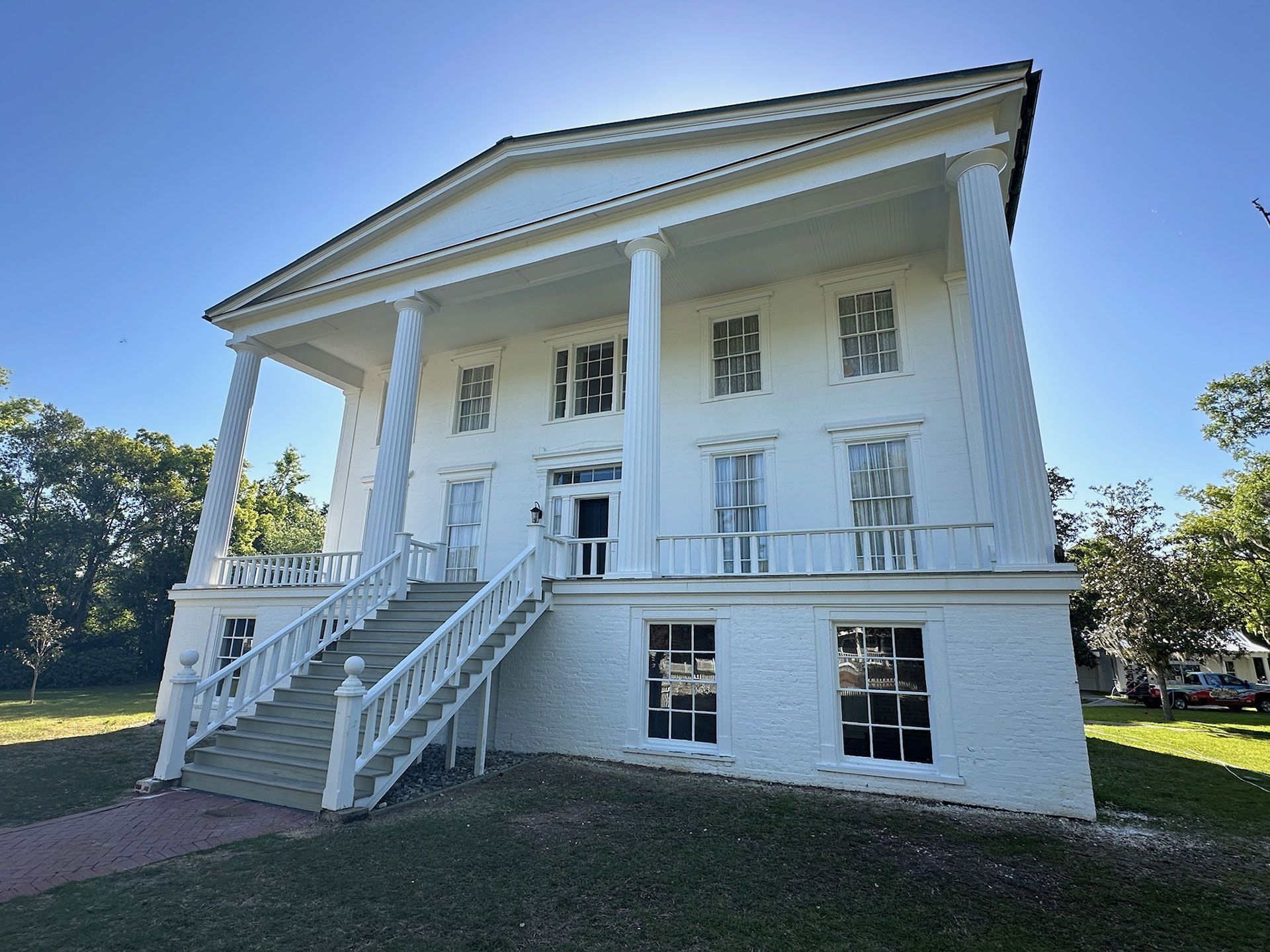 White historic house with columns, front stairs, and a porch on a grassy lawn under a blue sky