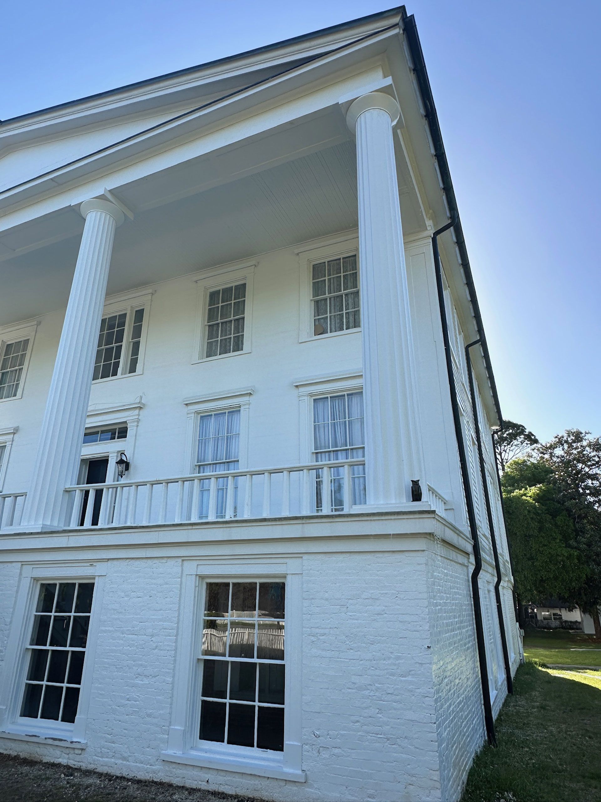 White two-story house with columns, balcony, and large windows in bright sunlight
