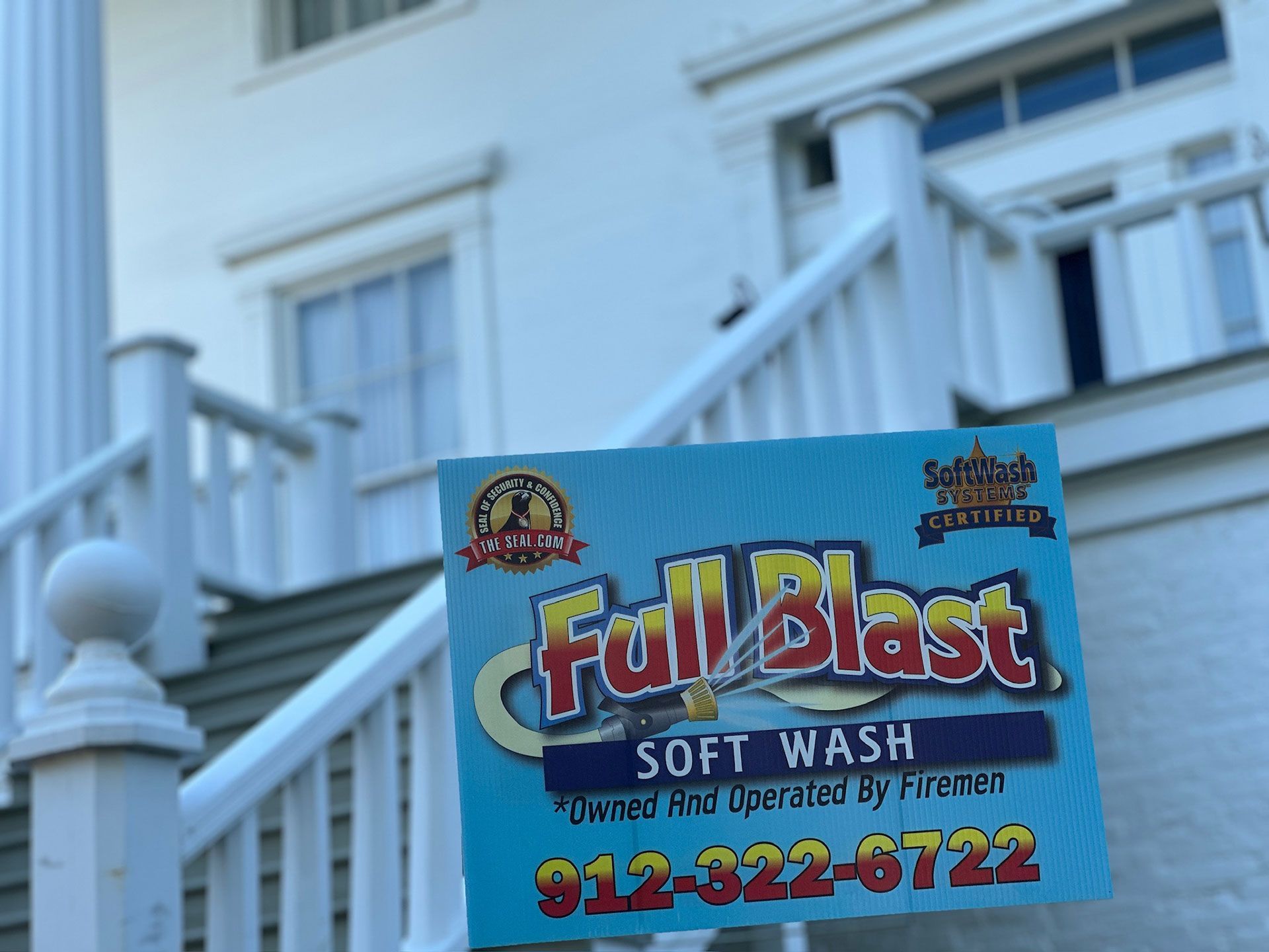 Blue “Full Blast” soft wash sign on a white porch railing with house siding in the background