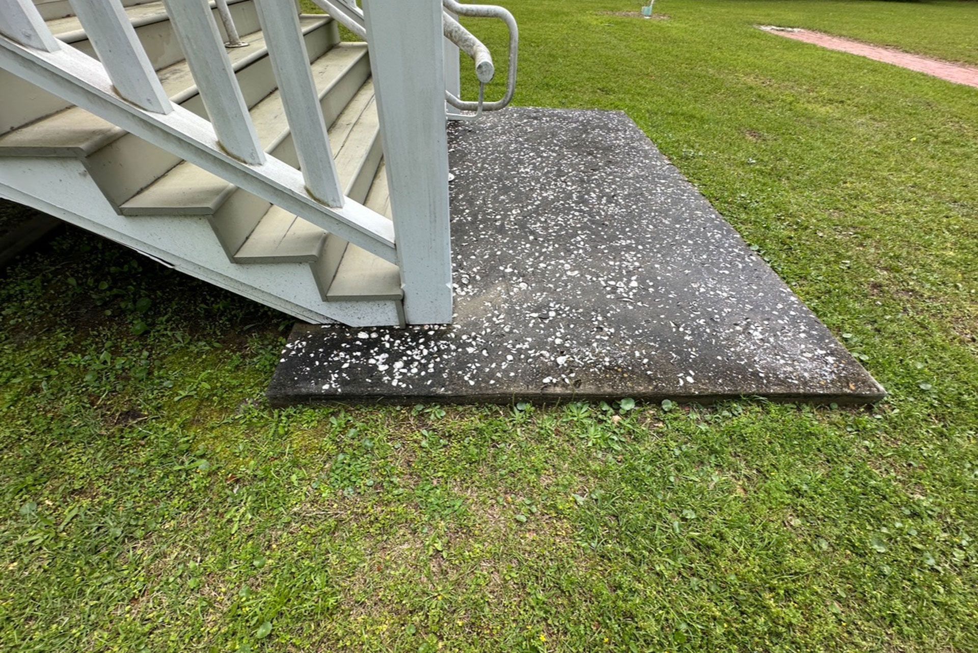 White wooden ramp beside a black mat on grass near a house porch