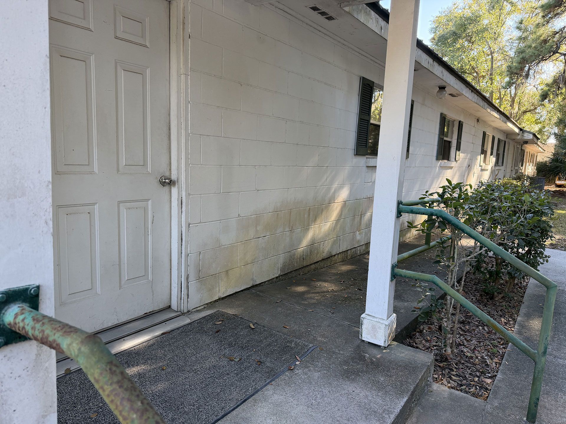 Exterior walkway beside a white building with a ramp, railing, and closed door