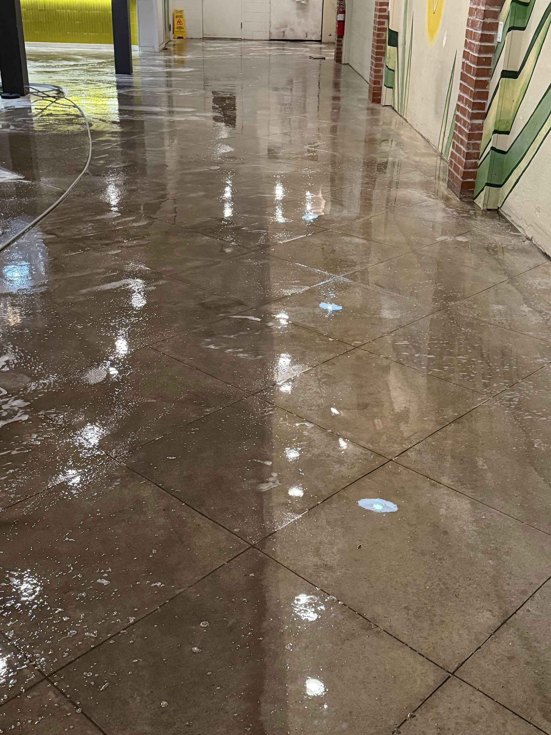 Water-covered tiled walkway with reflections and a painted wall on the right