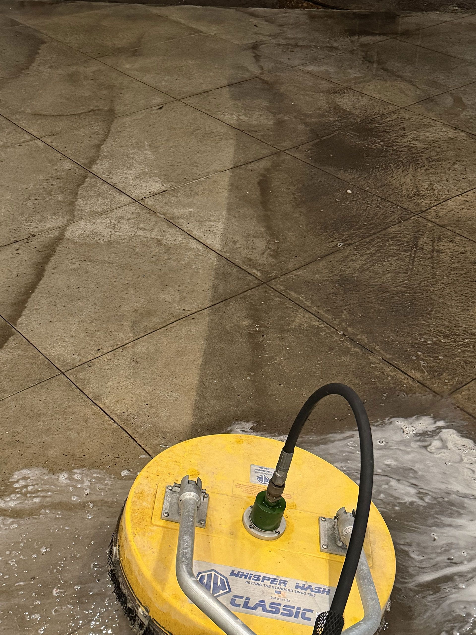 Yellow floor cleaning machine on a concrete surface with a black hose attached