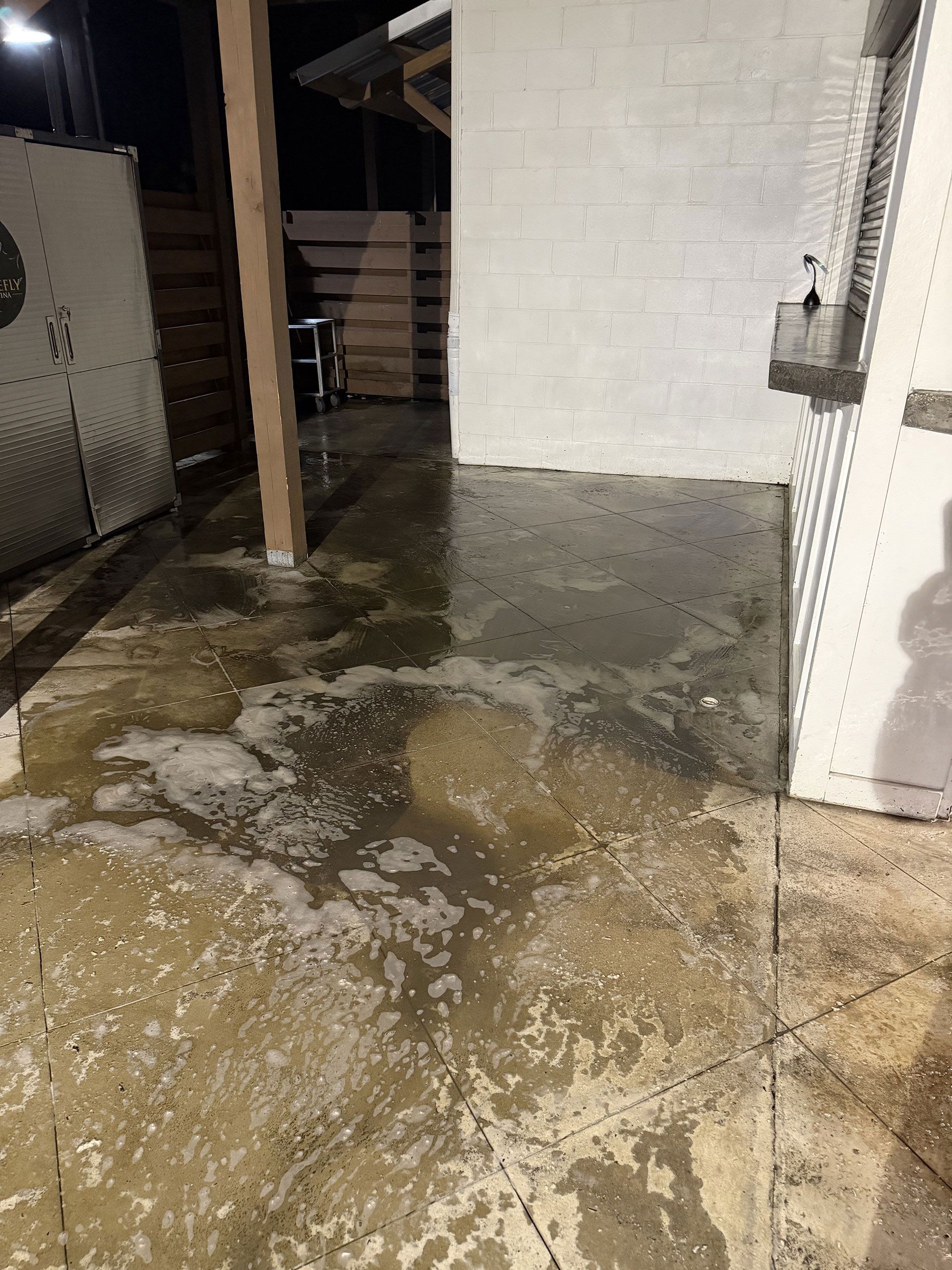 Wet concrete patio beside white brick wall and metal fence at night