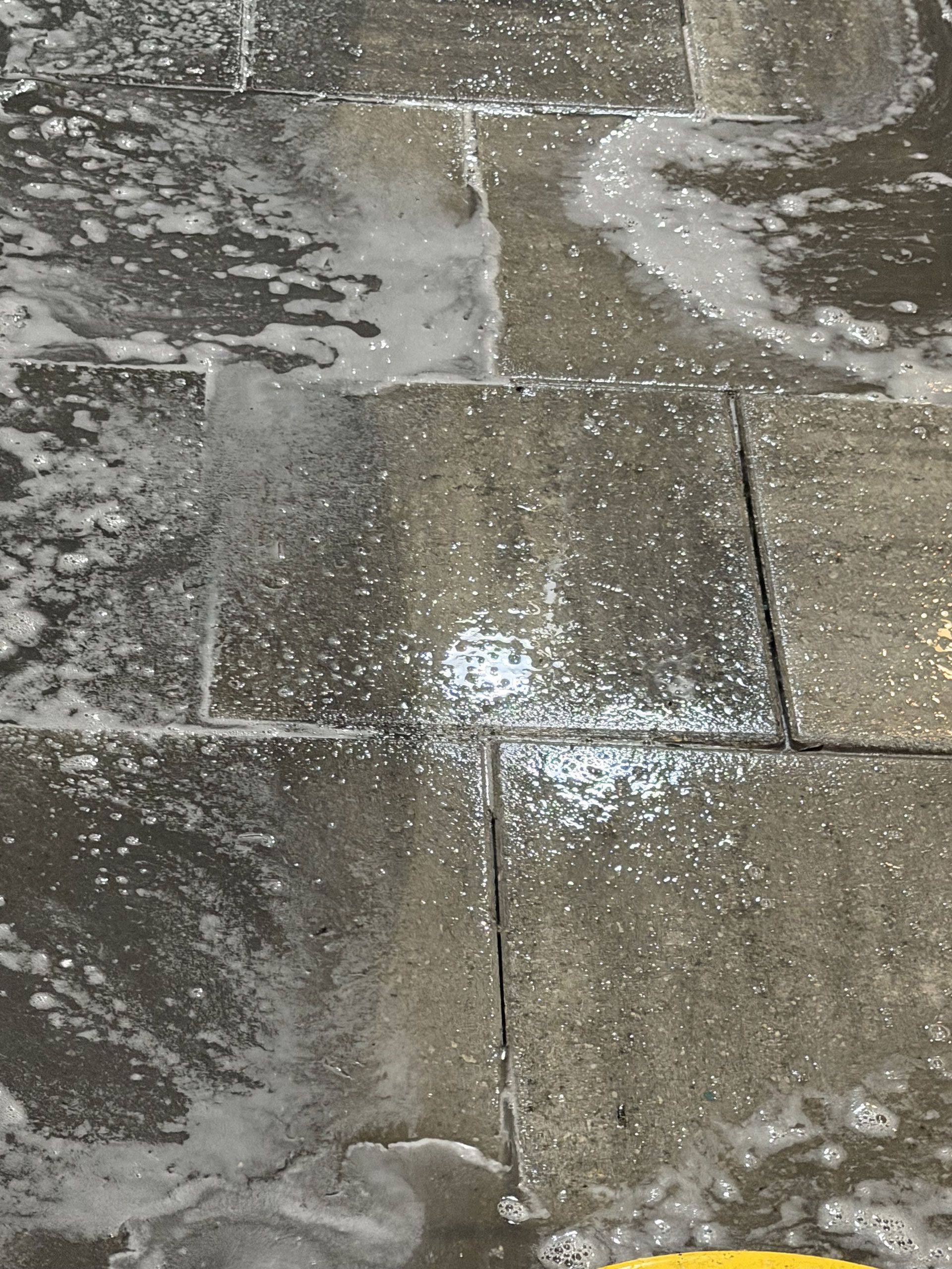 Wet stone pavement with white soap suds and patches of water.