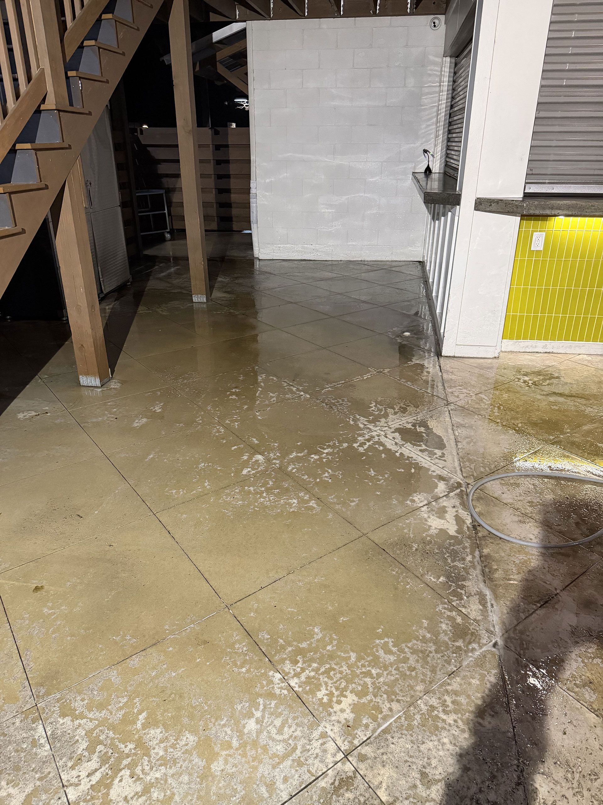 Indoor floor flooded with water near stairs and a doorway, with wet tile and debris.