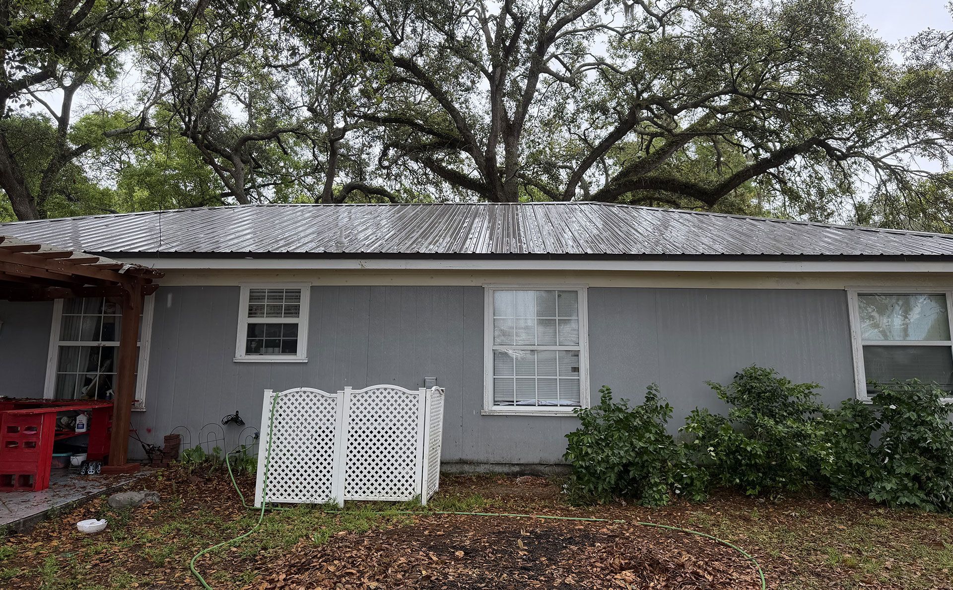 Gray house exterior with white trim, red porch posts, and a white fence panel in front under trees