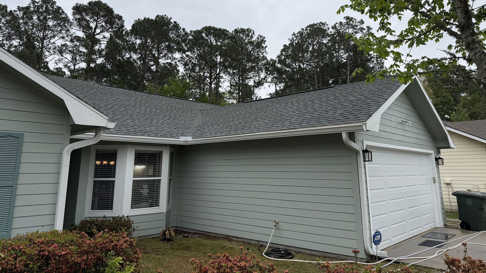 Suburban house exterior with gray siding, white garage door, and wavy roofline under cloudy skies